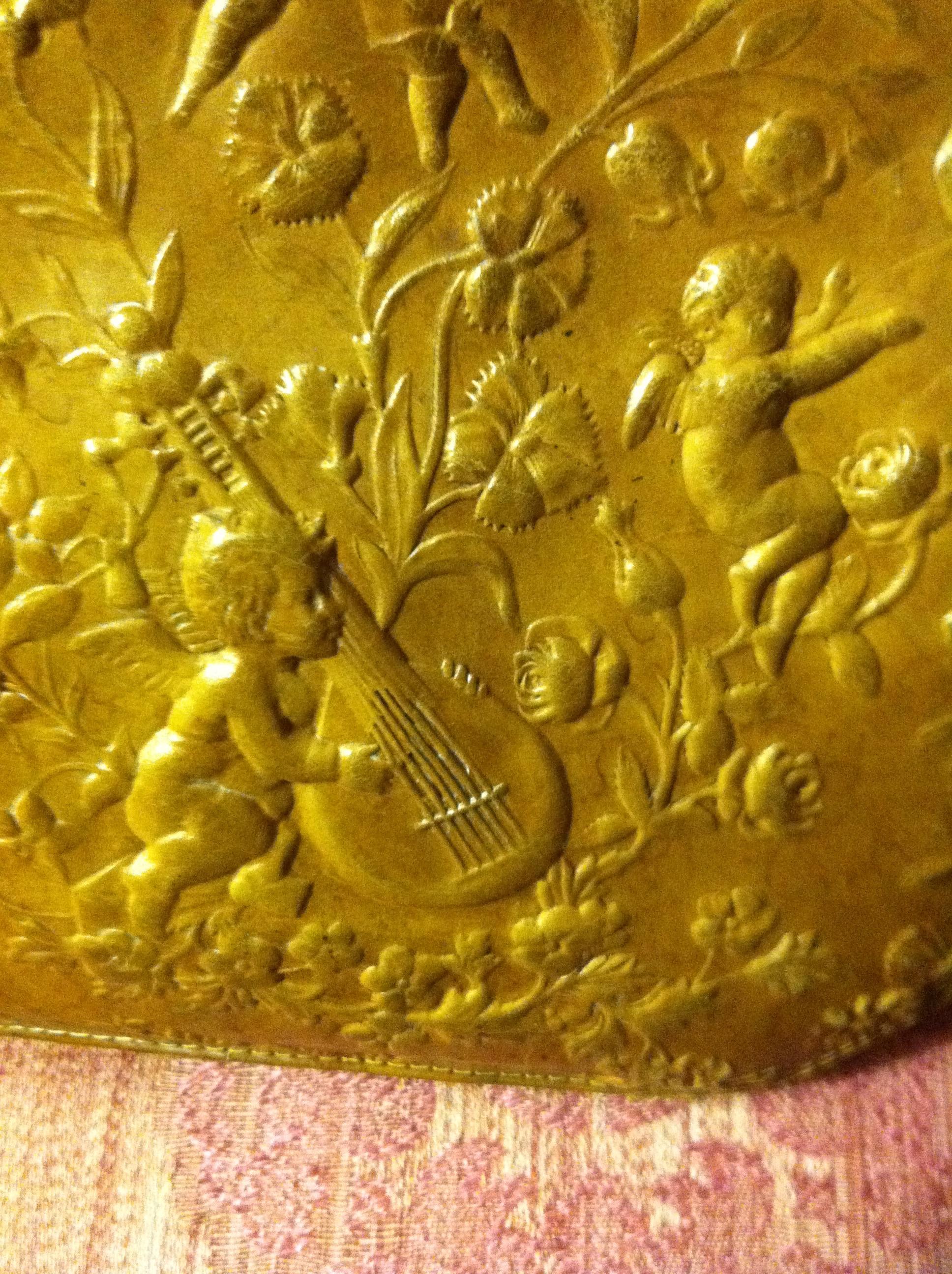 This Victorian leather embossed purse depicts a cherub playing a lute in the center, surrounded by floral elements, birds, and another cherub.  The embossed leather is caramel-colored and lined in silk of a similar shade. Both sides of the purse