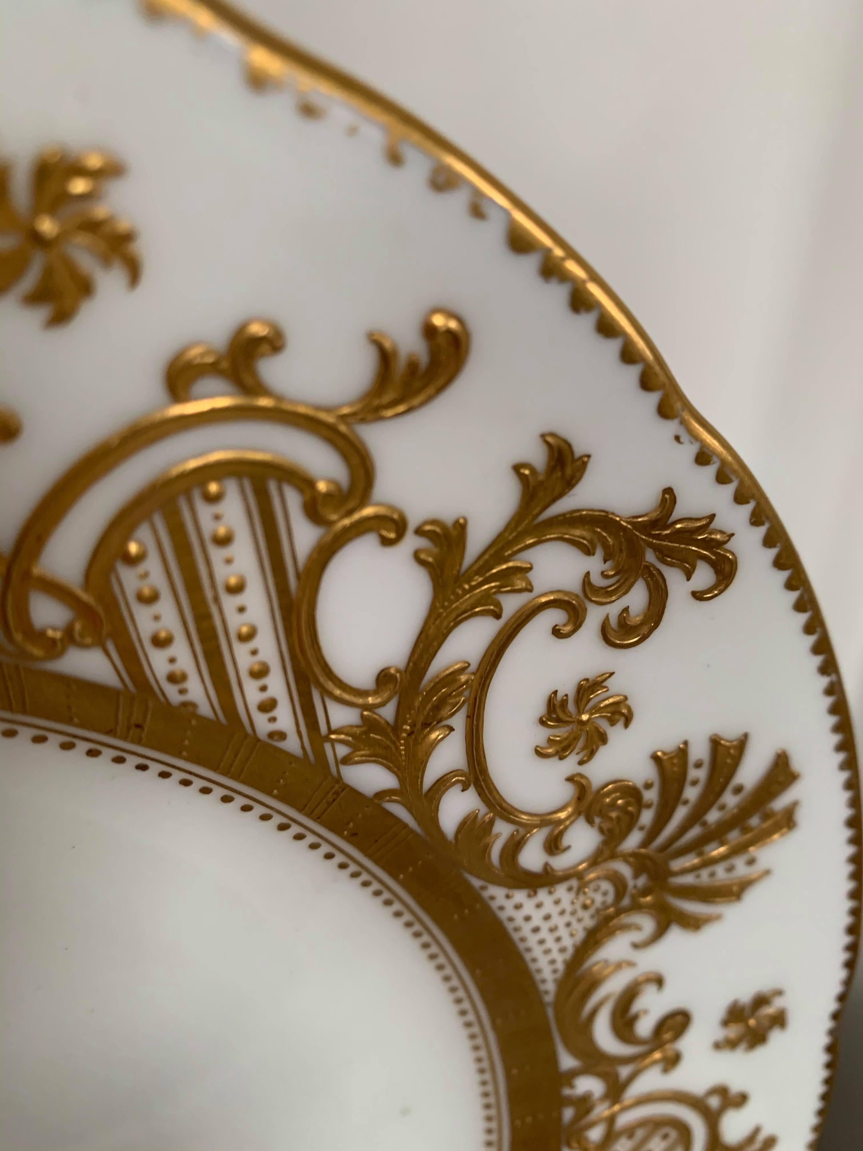 This porcelain plate with gold details is a beautiful decorative piece. Its regal hand-painted and gilded detailing is intricate and delicate. It is a Minton plate (C6482). Noted on the back of the plate, it was sold at world-famous Gilman Collamore