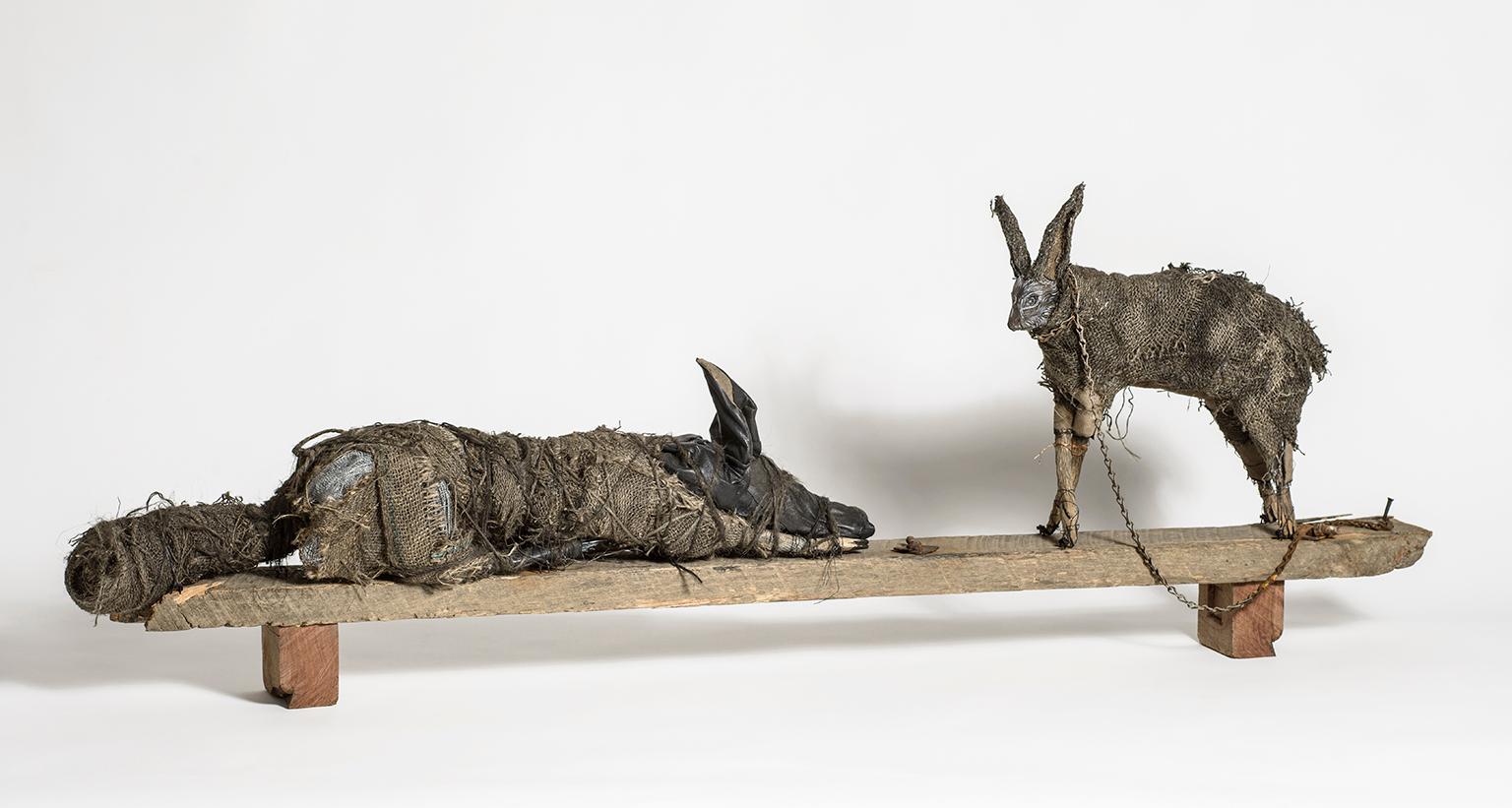 Elizabeth Jordan Figurative Sculpture - Sculpture of Rabbit and Dog on wood block, earth tone: 'Sisters'