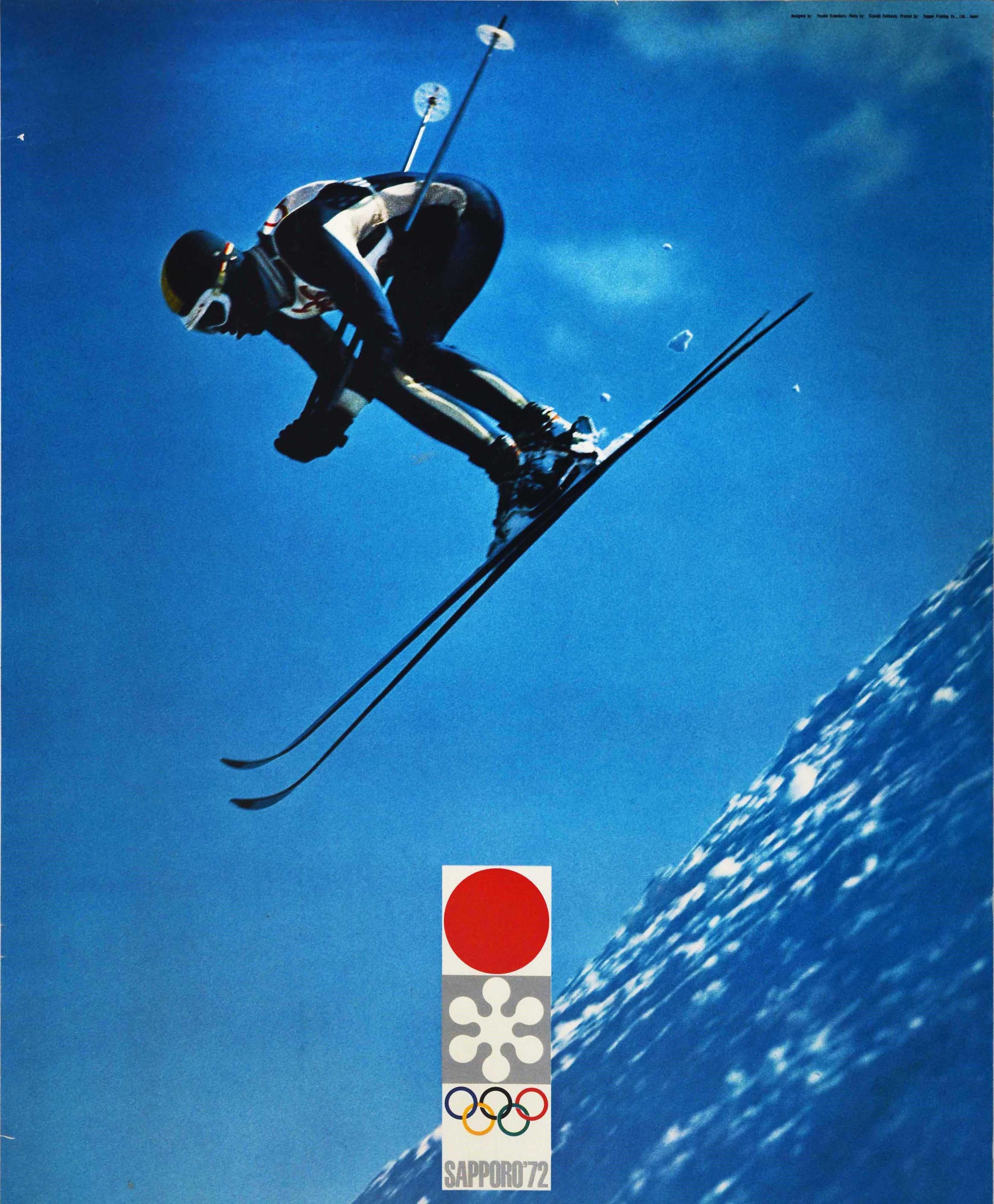 Original-Sportplakat für die XI. Olympischen Winterspiele, die vom 3. bis 13. Februar 1972 in Sapporo, Japan, stattfanden. Es zeigt einen Skifahrer, der mit hoher Geschwindigkeit über eine verschneite Piste springt, vor einem strahlend blauen Himmel