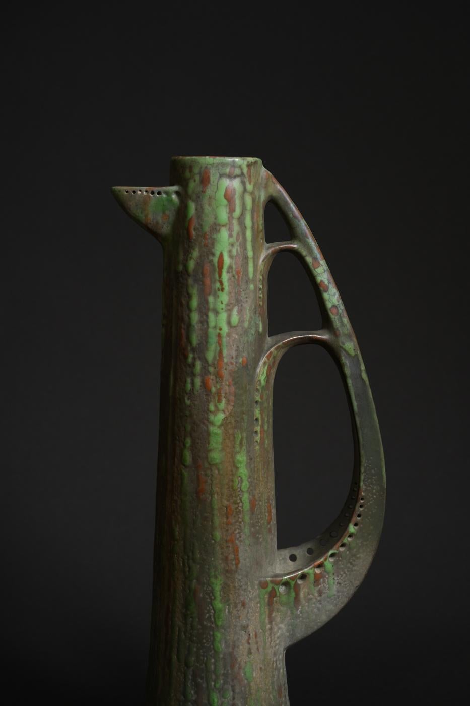 Austrian ceramist Paul Dachsel designed this unusually shaped pitcher, made of hard earthenware and covered in a light green glaze. Its slim and elongated body gives the piece an elegant look, accentuated by a highly stylized handle that evokes