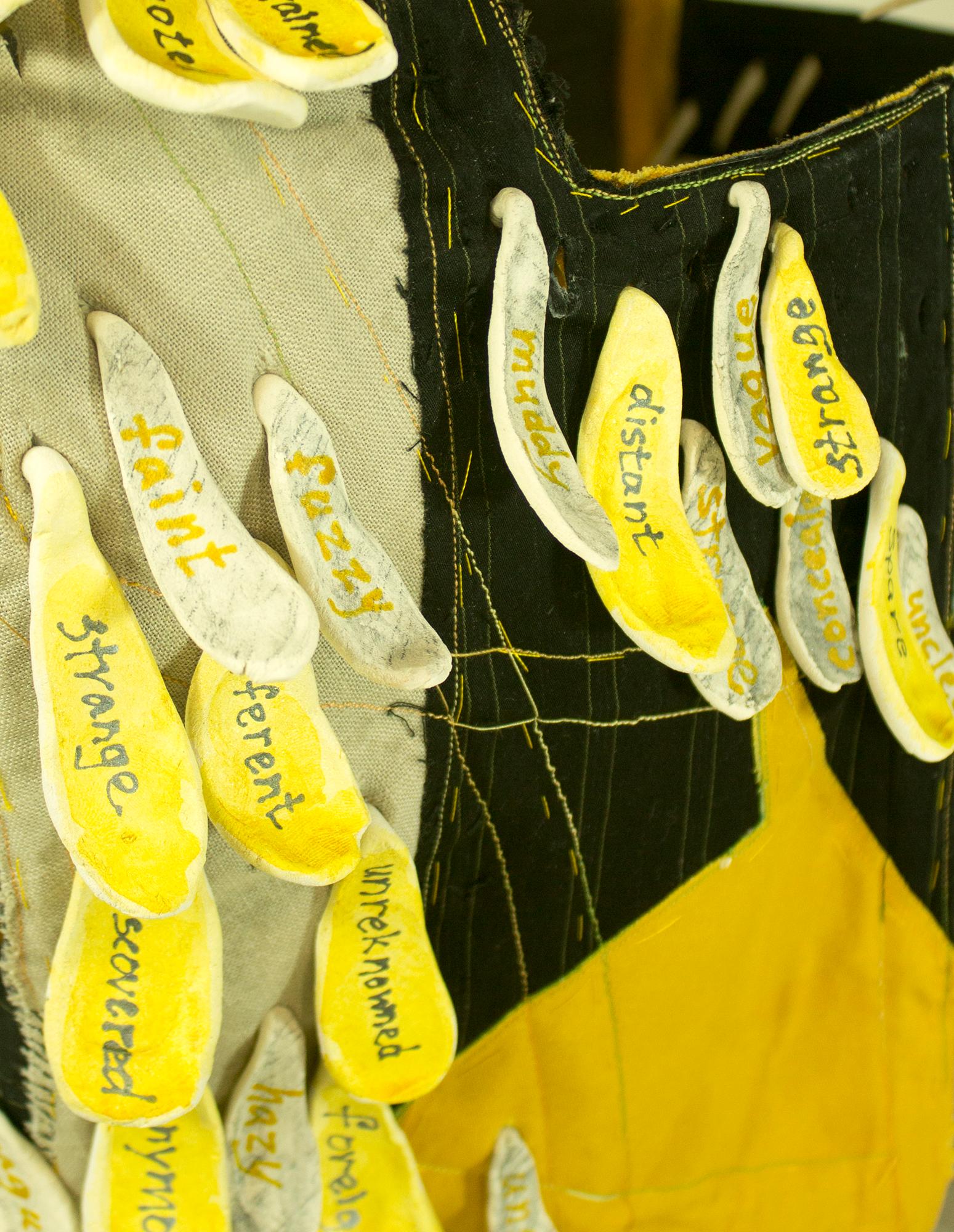 Virginia Mahoney’s “Caution” is a mixed-media sculpture in vest form, that is black with bright yellow accents, and has attached ceramic tags on which words referring to being cautious are handwritten. Ceramic spikes projecting inside emphasize the
