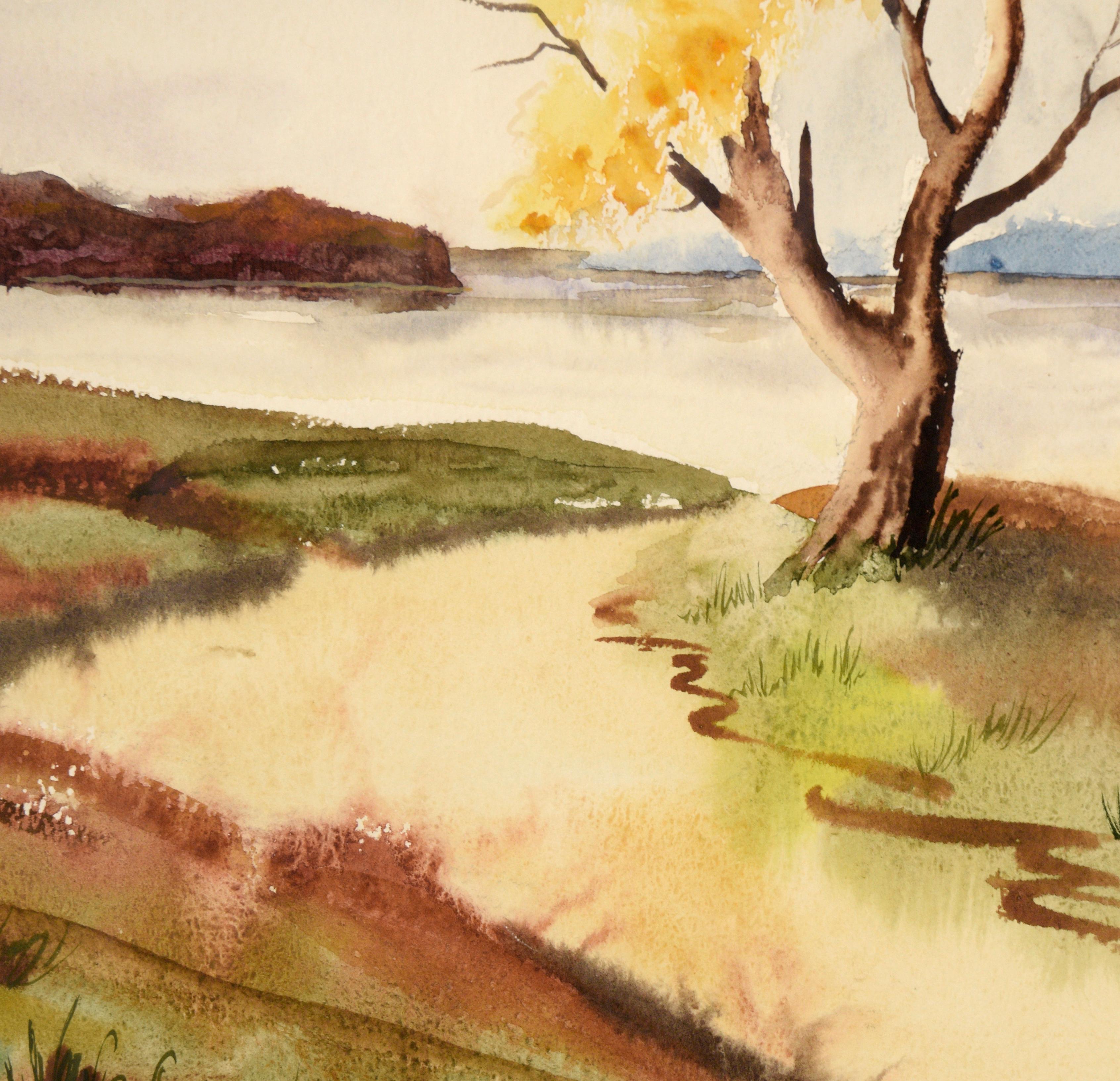 Serene watercolor by California artist Edna Lewis (nee Sutherland) (1905-1975). The viewer looks our over an inlet to a lake or bay, with mountain ranges in the distance. Two trees with bright yellow leaves sit at the shore of the water. The sky is