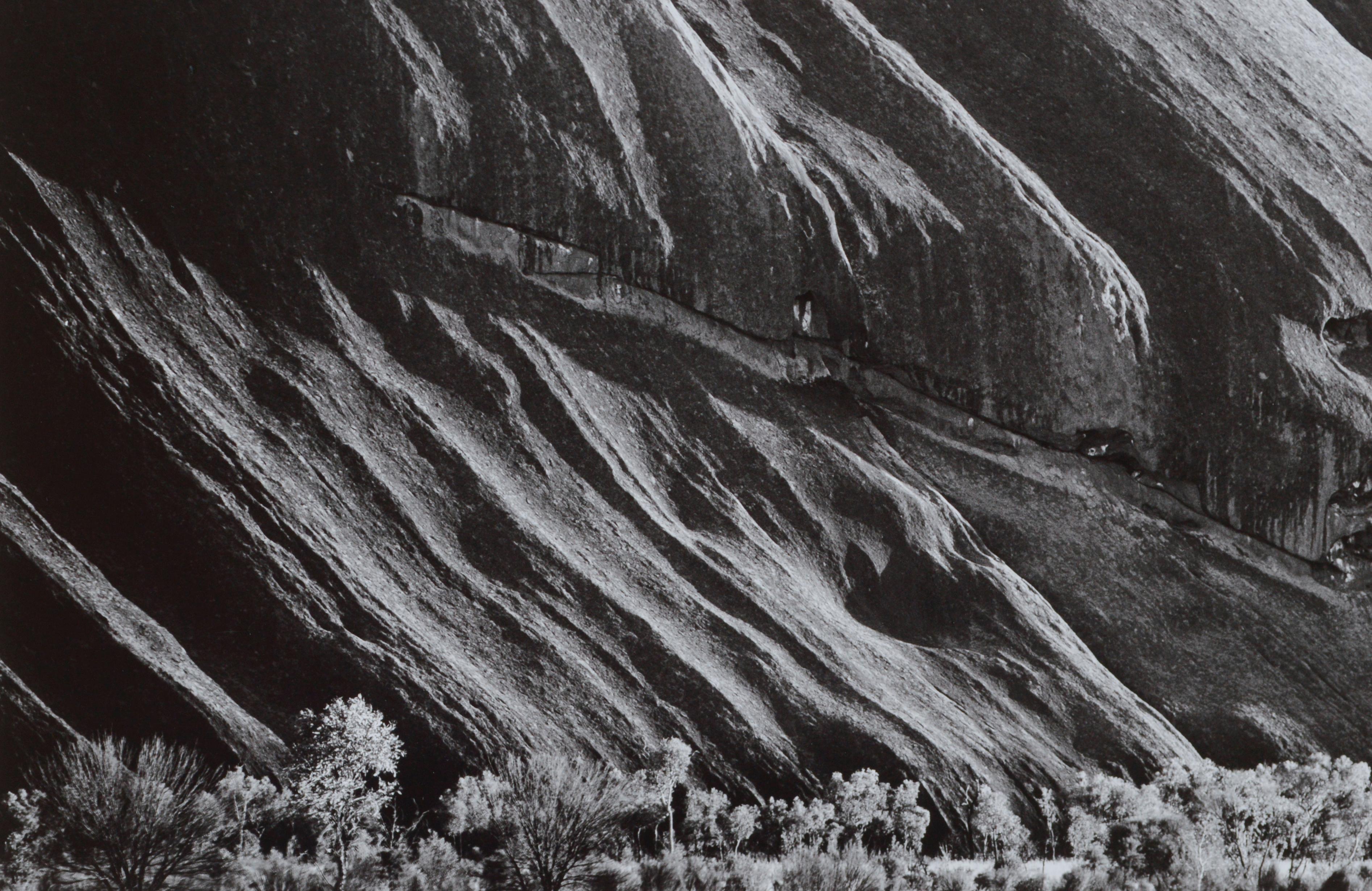 Behold nature's stunning beauty in this black & white hand signed landscape photograph of beautiful Ayers Rock in Australia, showcasing the elegant curvature of the dramatic cliffside and the its incredible scale juxtaposed to the small shrubs