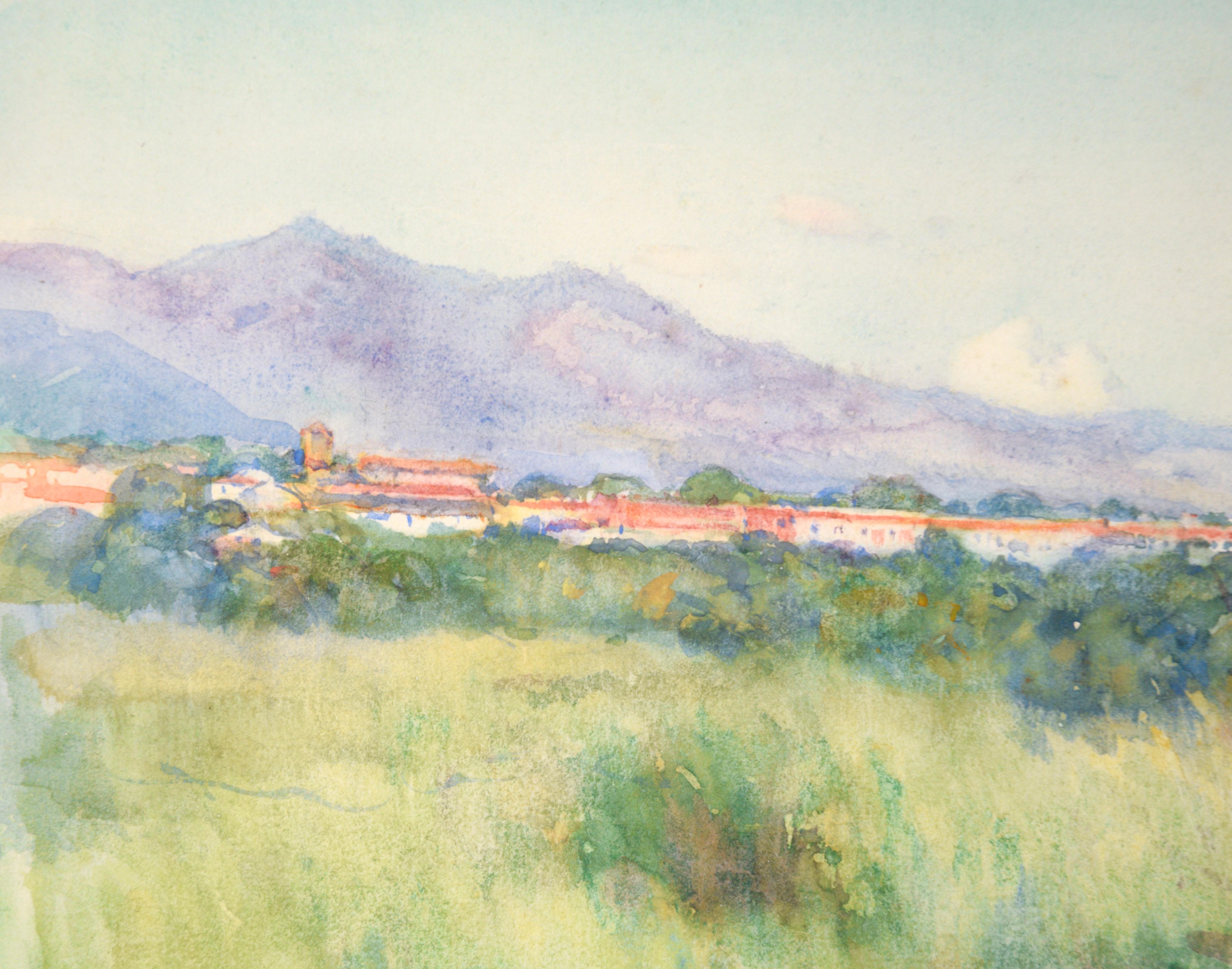 Idyllic watercolor of grassland and mountains in Cuba by Leonard Lester (English, 1870-1952). A large, grasy field stretches out from the viewer, lush and full of plants. At the far end there is a small group of buildings with red roofs. Beyond the