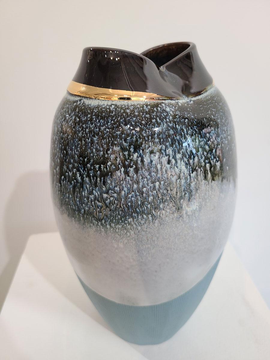 This small ceramic vessel by Connecticut-based ceramicist, Jon Puzzuoli, is made with glazed turquoise porcelain. The base is a light, textured blue color, with a two-tiered glaze that covers the top half of the body. A translucent white and deep