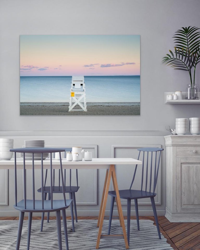 This contemporary coastal photograph by Peter Mendelson captures a sunny, summer day on a New England beach at sunset. A white lifeguard stand sits on textured sand at the center of the composition, overlooking an ocean that fades to white at the