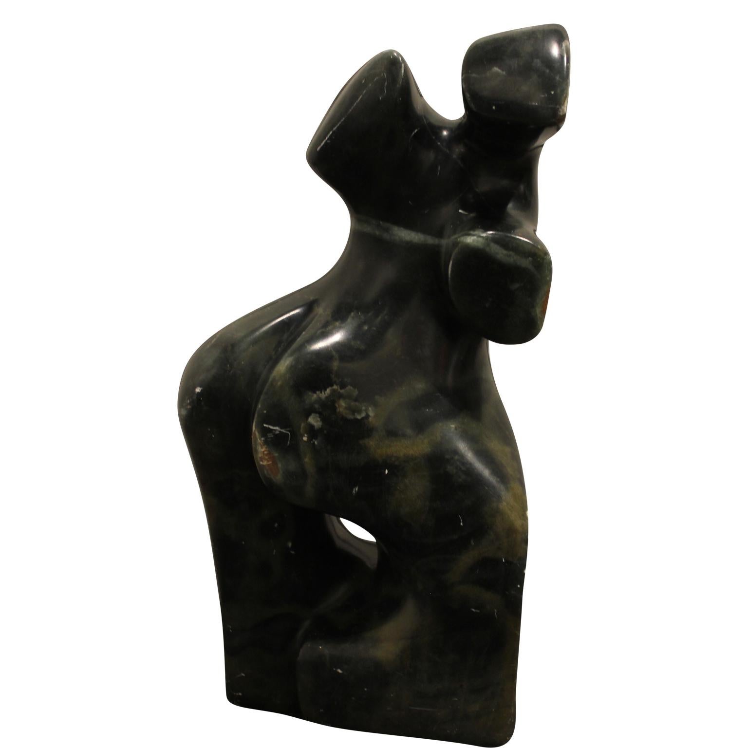 Dark jade colored sculpture of a female's torso with a white triangle meant to be the pubic triangle. The figure appears to be in movement. It has veins of lighter toned stone throughout the sculpture. 