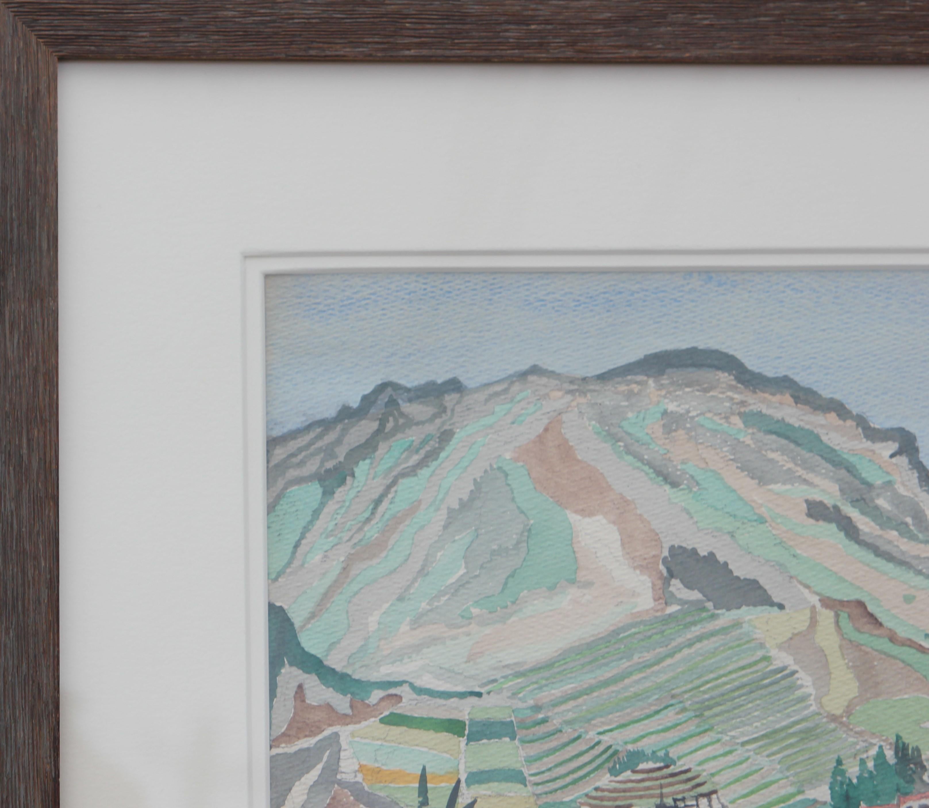 Pastel blue and green toned watercolor painting of a sweeping seaside landscape. In the distance a small town can be seen nestled amongst the mountains at the water's edge. Signed 