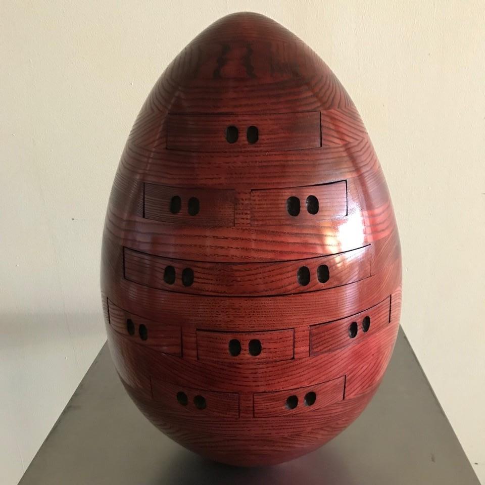 This hand carved wood egg sculpture features nine functional drawers.  The surface is smoothed to a perfect egg shape and is stained with a red varnish.  The drawers are an ideal place to store treasured items sitting atop a table or dresser.  In a