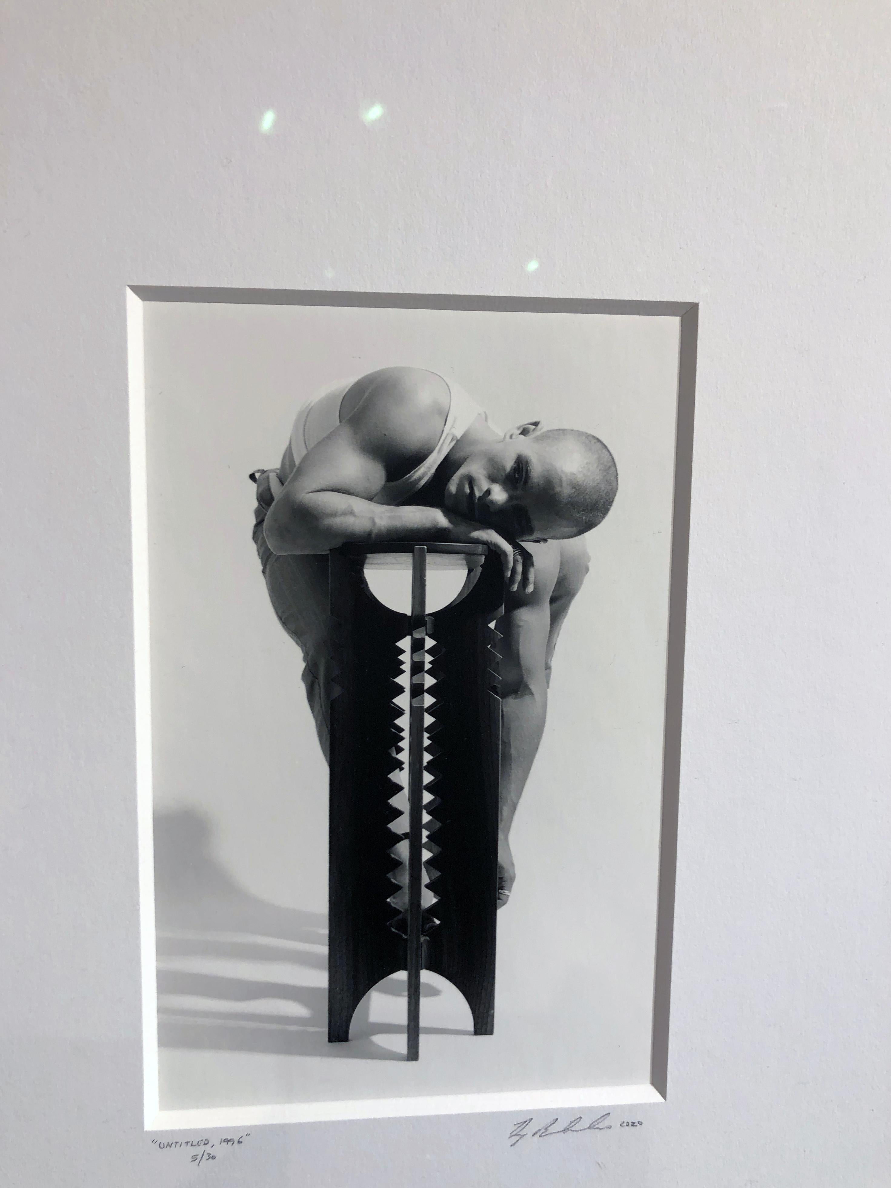 Male nude figure draped over contemporary architectural table.  .  The artist uses traditional photography methods shooting the image on film.  The image is printed using traditional darkroom techniques.  The artwork is tastefully framed and matted.