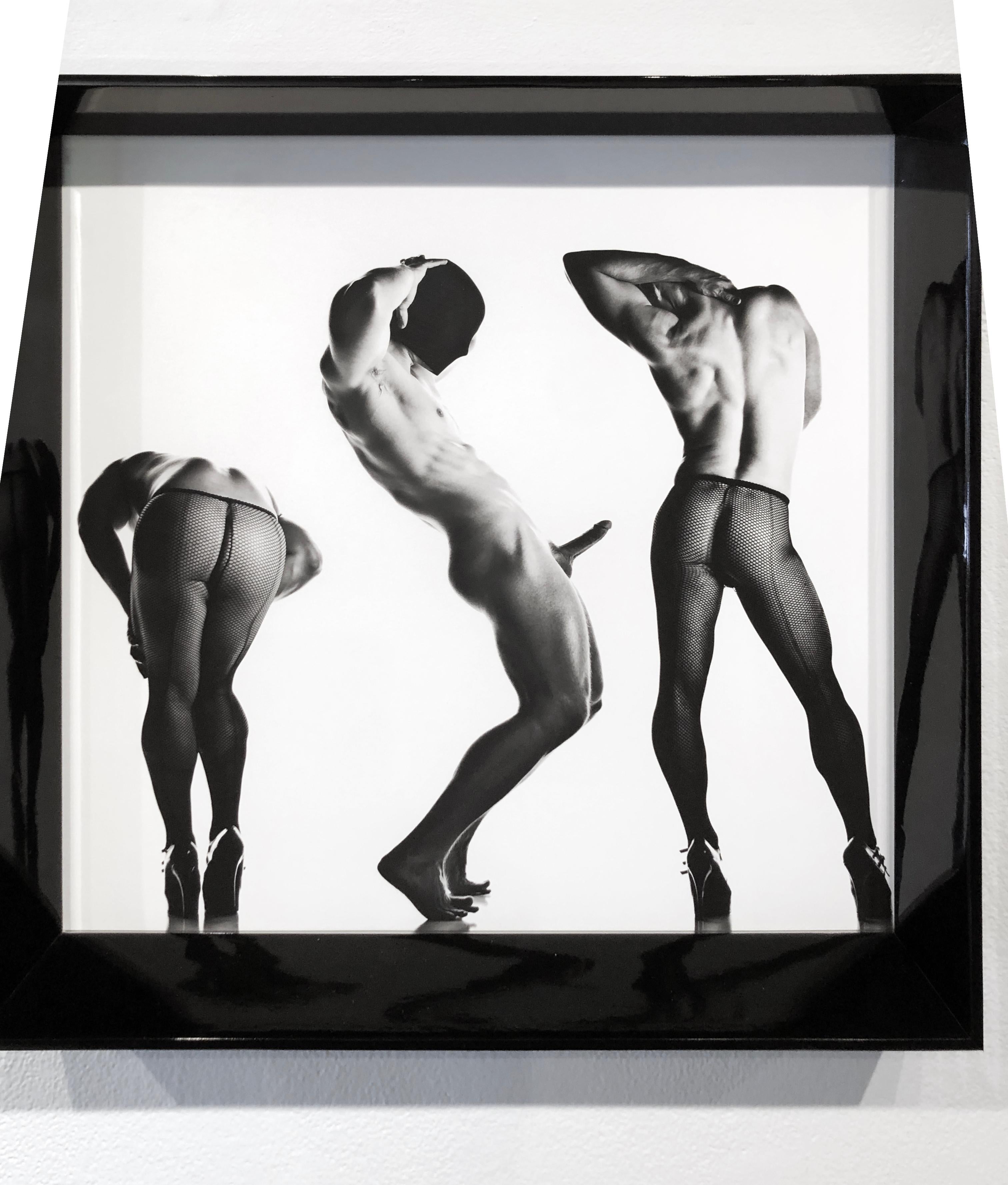 This is a triple portrait of a muscular male in three different poses and dressed only in fishnet stockings and stiletto heels.  The model is dramatically lit and poses seductively for the camera.  His arousing contortions of the body appear to