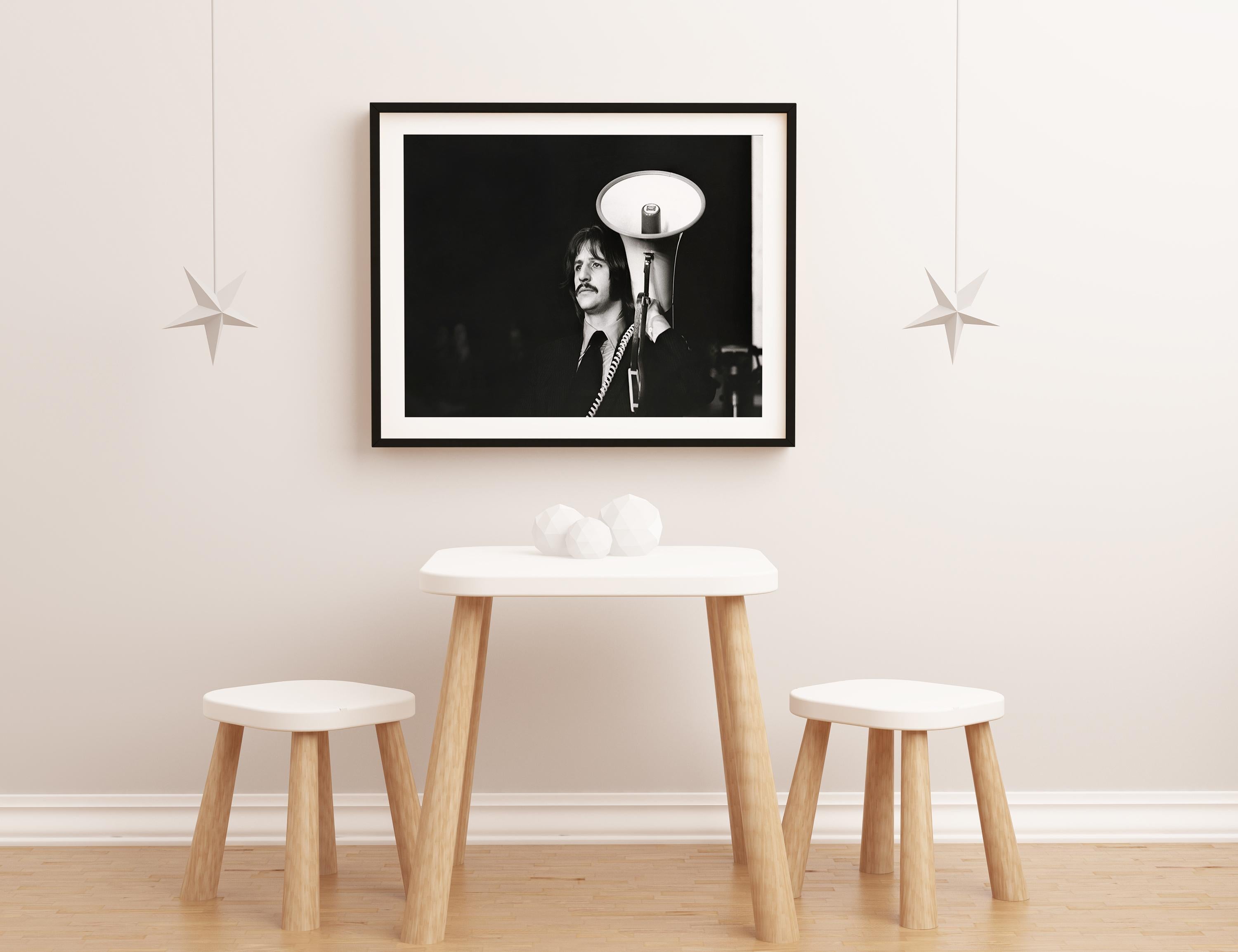 This black and white portrait features Ringo Starr of the Beatles holding a megaphone.

Ringo Starr is an English musician, singer, songwriter, and actor who gained worldwide fame as the drummer for the Beatles. He occasionally sang lead vocals,