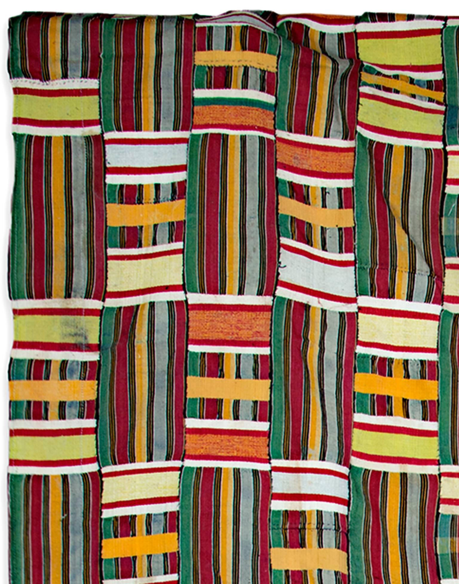 This cotton fabric was made by an unknown Ewe artist. It features red, blue, gold, and green accents. The Ewe people are an African ethnic group. This may be an example of Kente, a type of silk and cotton fabric made of interwoven cloth strips and