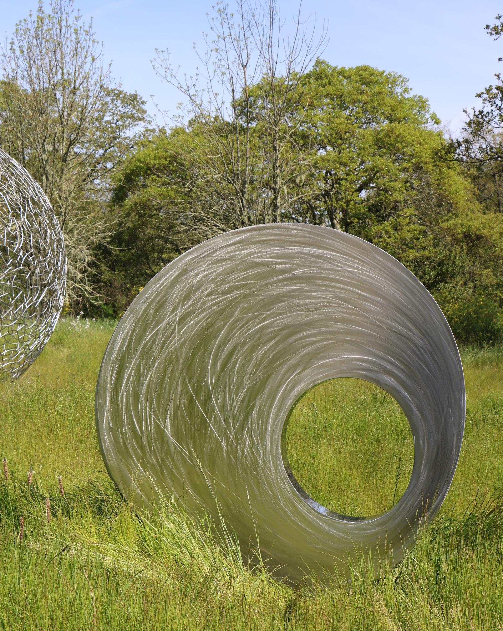 This stunning interactive kinetic sculpture in stainless steel easily rotates when pushed by hand. The outside surfaces have emphasized grinding marks that contrast beautifully with the highly polished hole in the middle. 

Dimensions shown are the