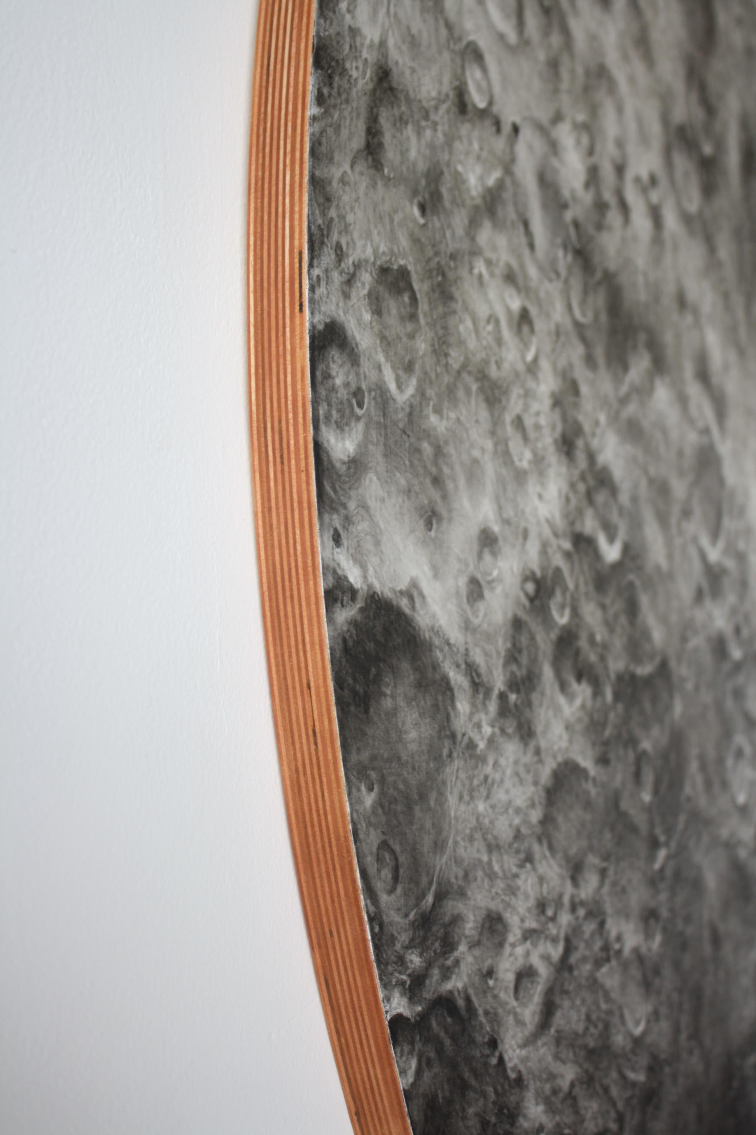Bethany Carlson's photo-realistic charcoal drawing on a round panel. The image is of a moon or a planet in space.  More information below:

While thinking about the nature of a moon, I created works that reflect the gentle tug our moon has on our