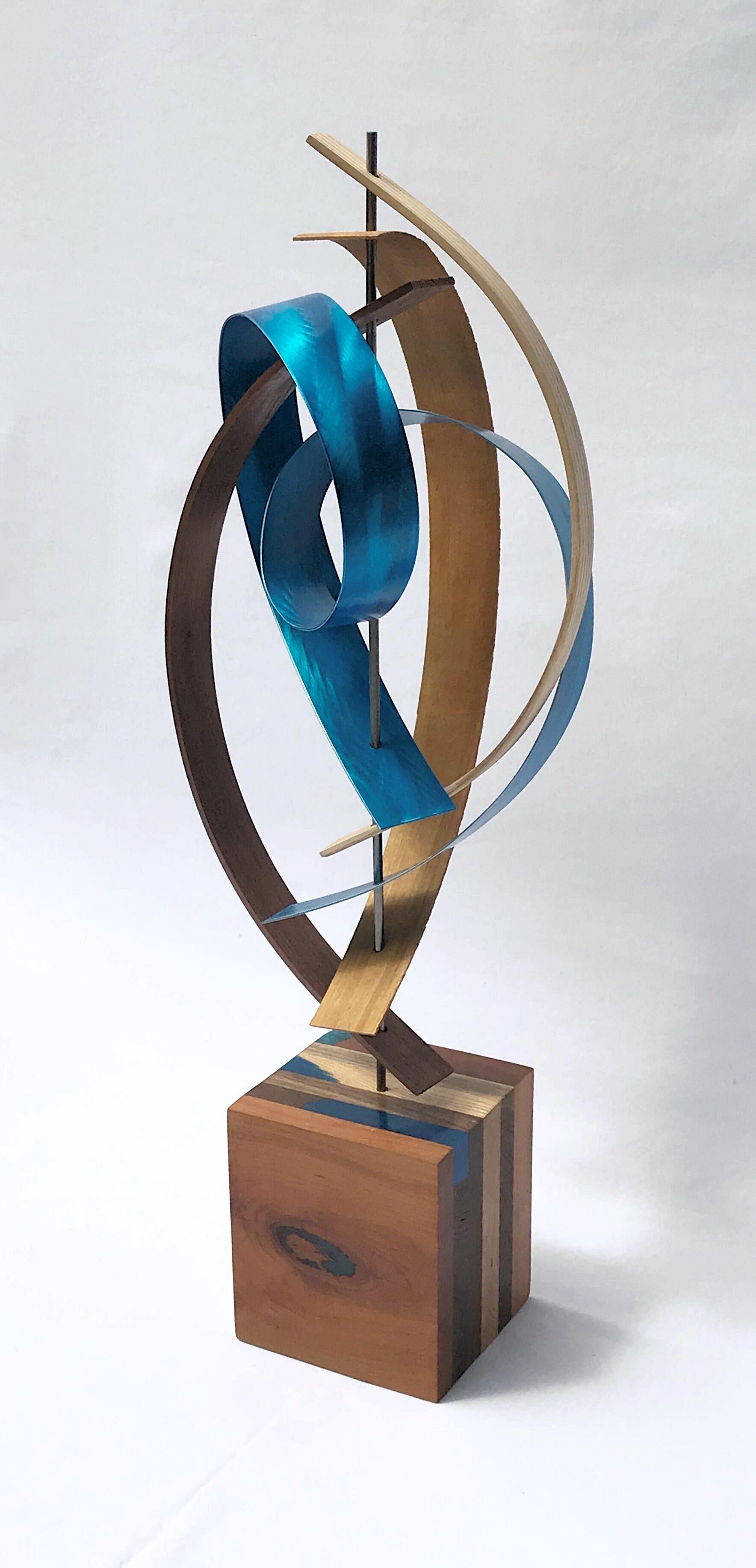 Titel: B-Schleife 
Beschreibung: Kirsche:: Nussbaum:: Esche:: gebogen und geflochten über einer Stahlstange:: die mit einer blauen „ribbonartigen“ Aluminiumlatte mit Schmelzmuster ineinander verschlungen ist. Der Sockel ist eine Verlängerung der