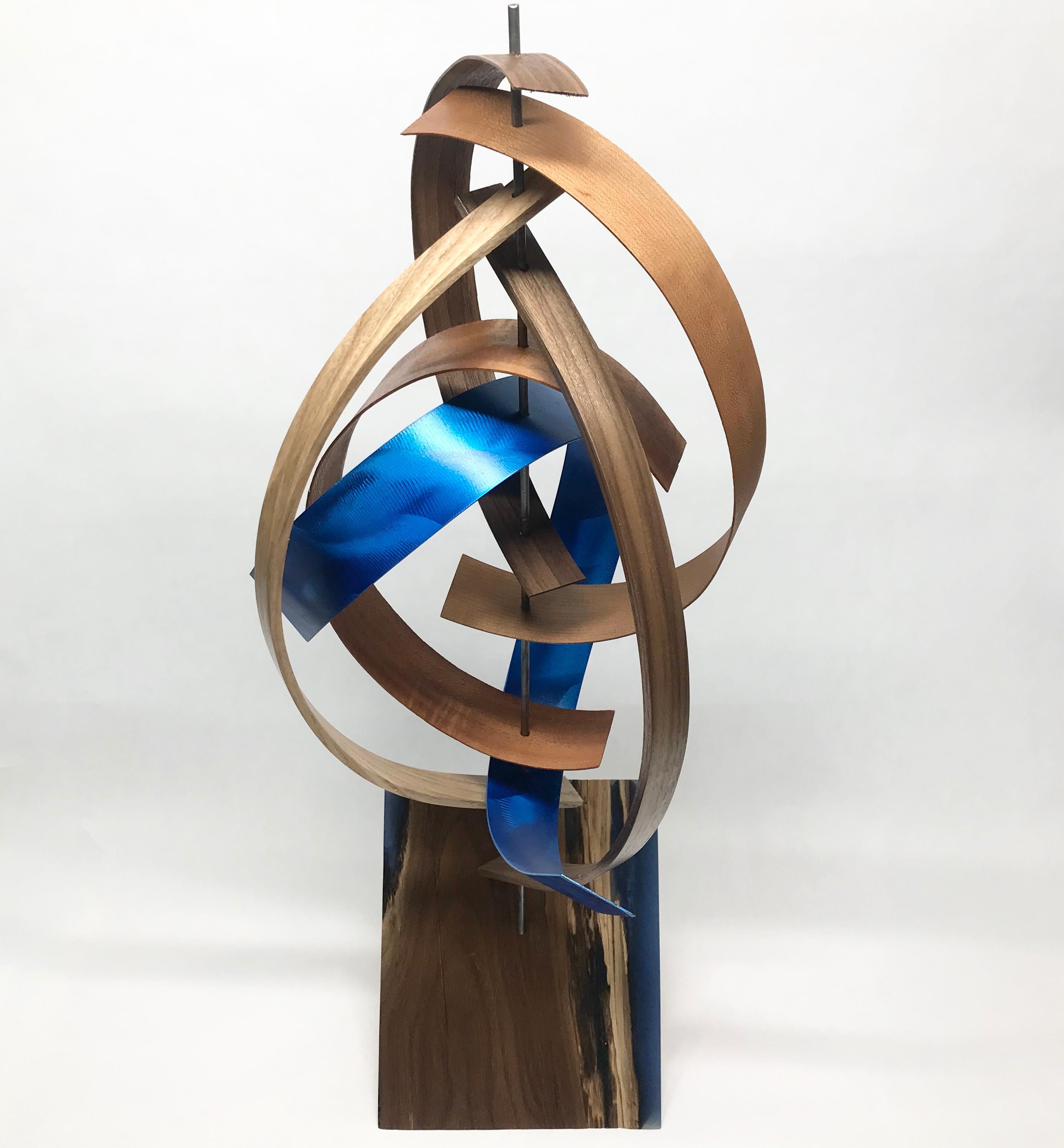 This Mid-Century Modern Inspired Wood Sculpture is comprised of black walnut and mahogany slats along with a ribbon of  blue hand-ground, hand-painted aluminum. The black walnut base is accented with blue epoxy inlay. 
Title: Streak
Artist: Jeff