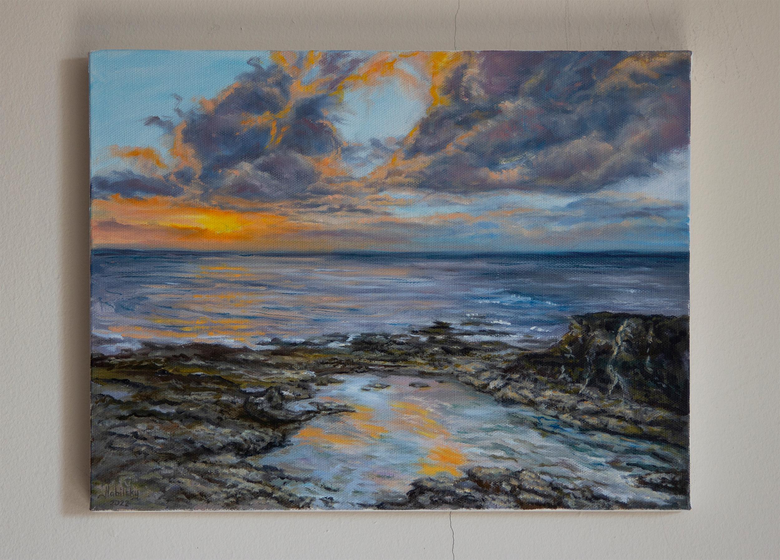 <p>Artist Comments<br />A soothing ambiance falls on a rocky coastline. The setting sun gradually pulls away from the blue sky leaving touches of brilliant, orange light. The ocean mirrors this beautiful transition, filling the scene with warmth and