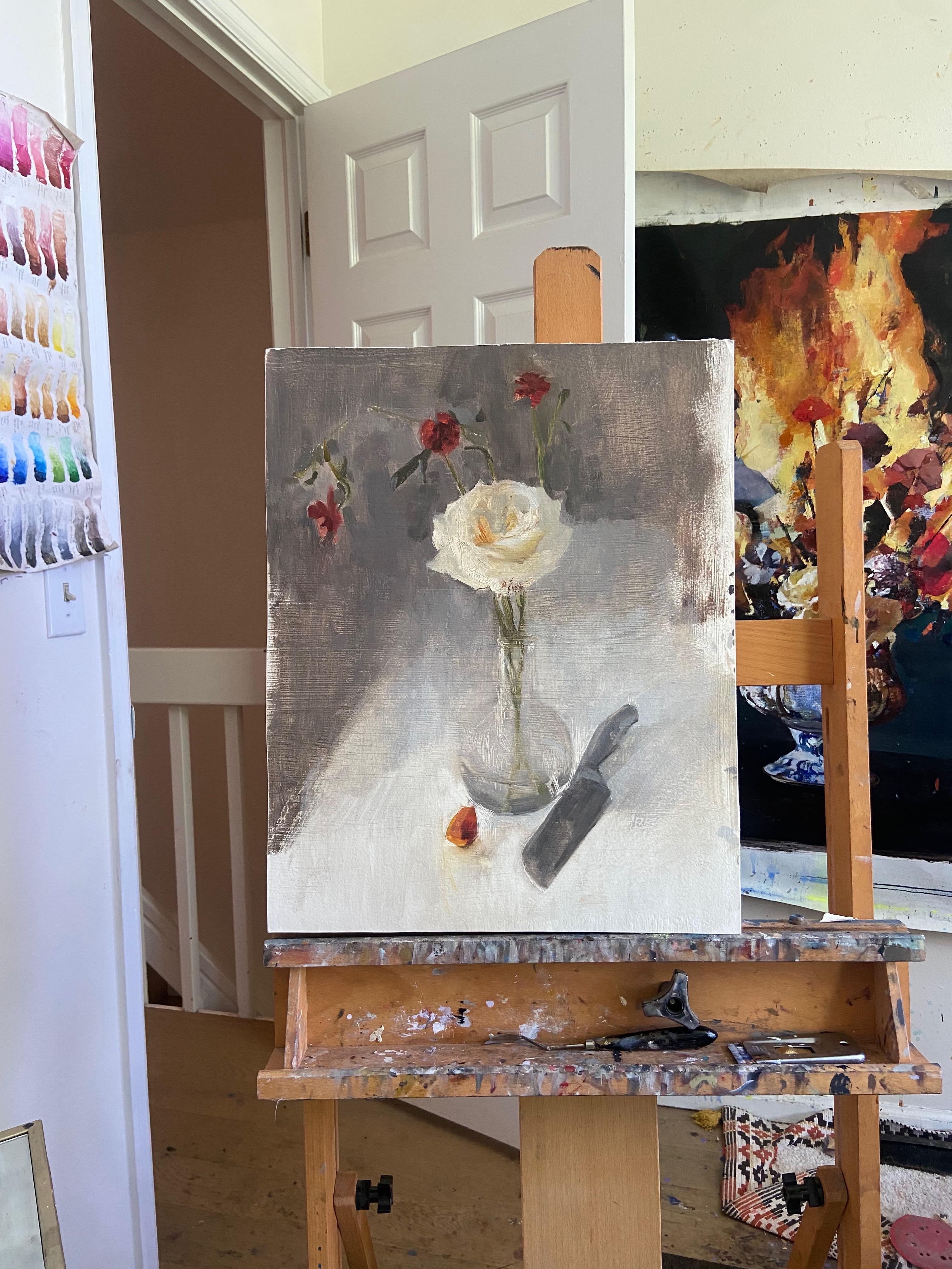 <p>Commenti dell'artista<br>Una natura morta dipinta a olio cattura un vaso trasparente che contiene una singola rosa bianca e tre rosse. Un coltello e un petalo caduto sono appoggiati accanto alla composizione floreale, aggiungendo uno strato di