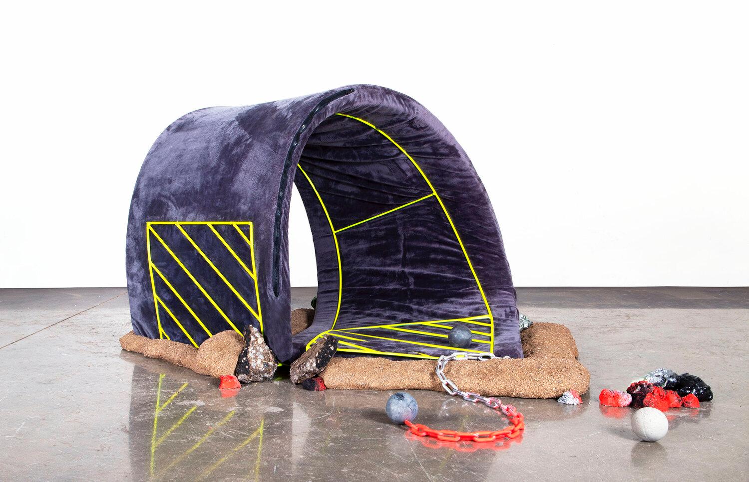This sculpture by Kenzie Wells was created for an exhibit titled Gradience. A plush roadway bends in an impossible manner, creating a loop. Yellow lines designate parking spaces on this surrealist road. Small 