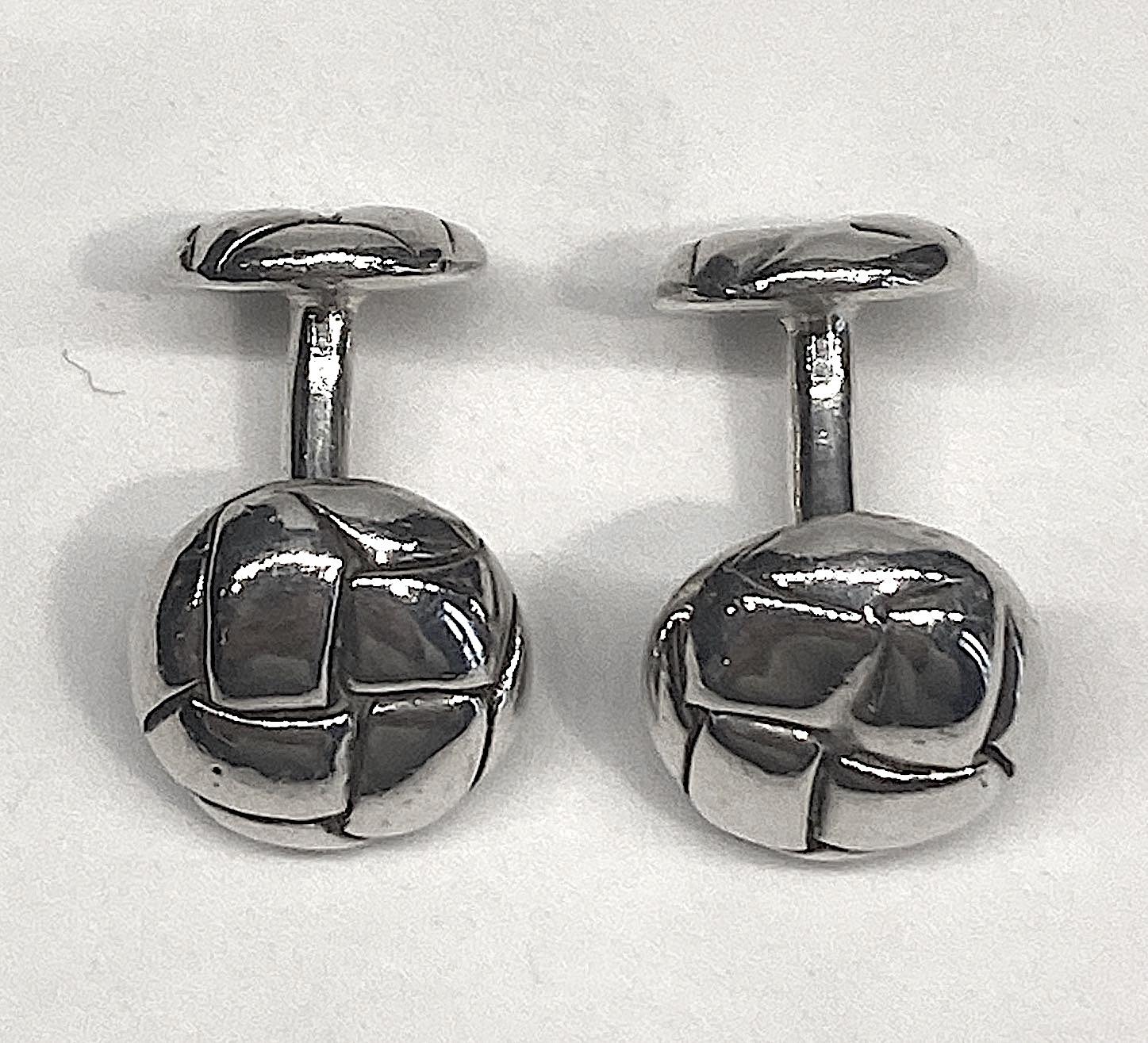 An elegant pair of sterling silver Angela Cummings barbell style cufflinks from 1985. The design on the front and back is inspired from woven leather buttons on a blazer. The front is .5 of an inch in diameter and the back is .44 of an inch in