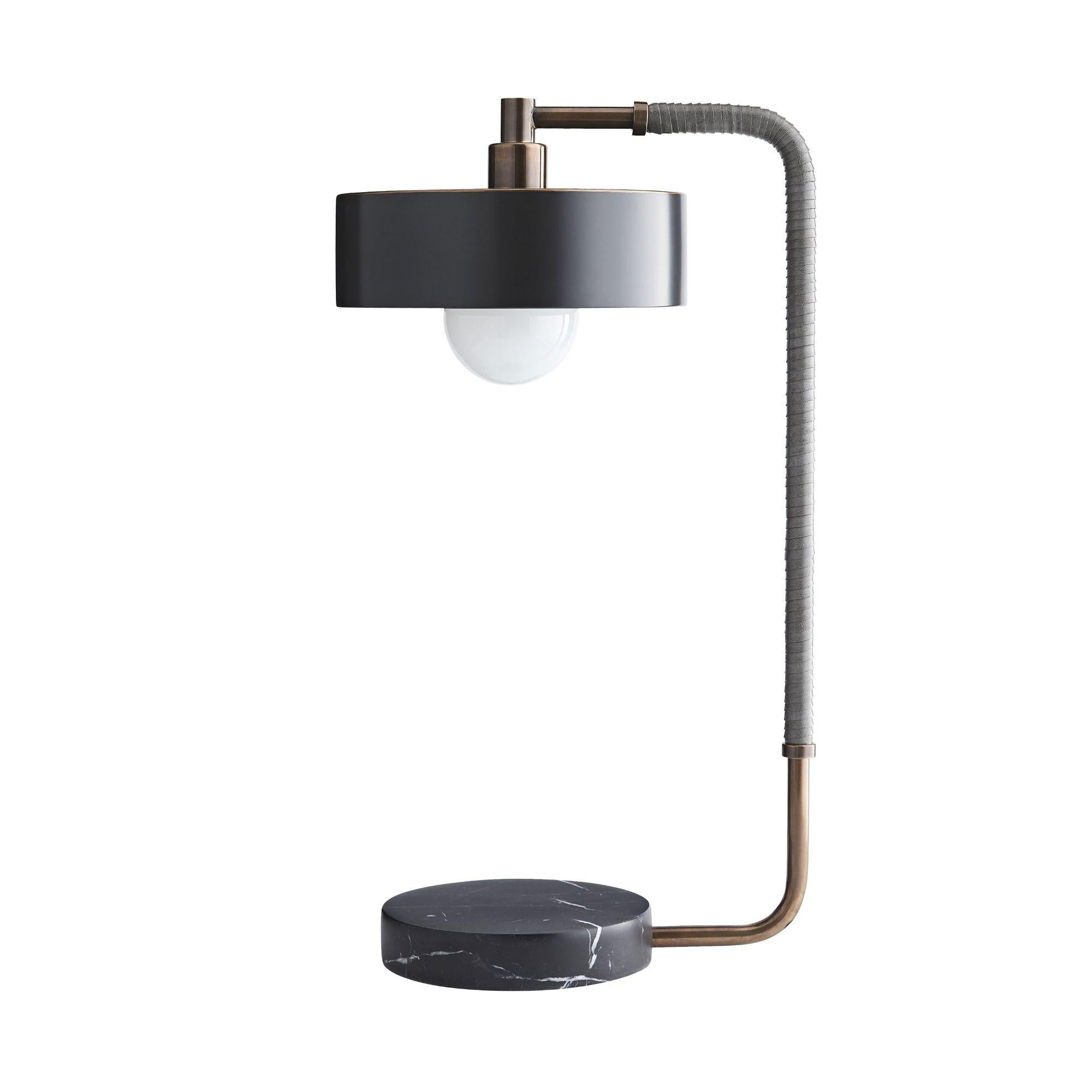 Alliant l'élégance contemporaine à des matériaux raffinés, la lampe Eleg est une pièce d'apparat définie par sa sensibilité épurée et moderne. Le cadre en acier laiton, enveloppé de cuir gris, se fond dans un socle circulaire en marbre noir, créant