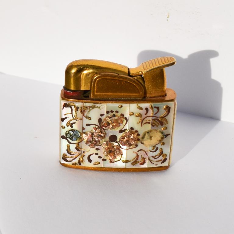 Petite embellished table cigarette lighter by Evans Fuel. A beautiful small lighter with brass top and bottom, and pearl and abalone inlay. Tessellated pearl is encrusted and decorated with hand painted flowers in bronze and deep maroon color.
Made