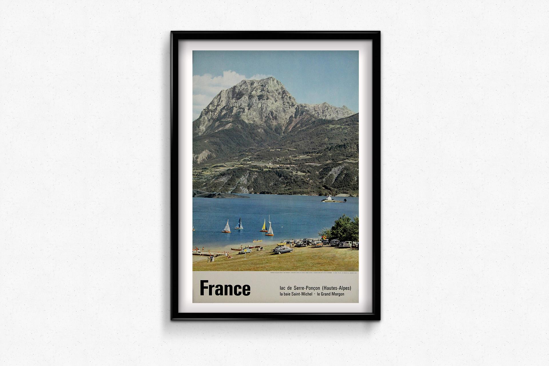 This vintage 1962 travel poster, photographed by Abeil, showcases the stunning Lac de Serre-Ponçon, a vast artificial lake in the Hautes-Alpes region of France. The image captures a lively summer scene with sailboats gliding across the deep blue