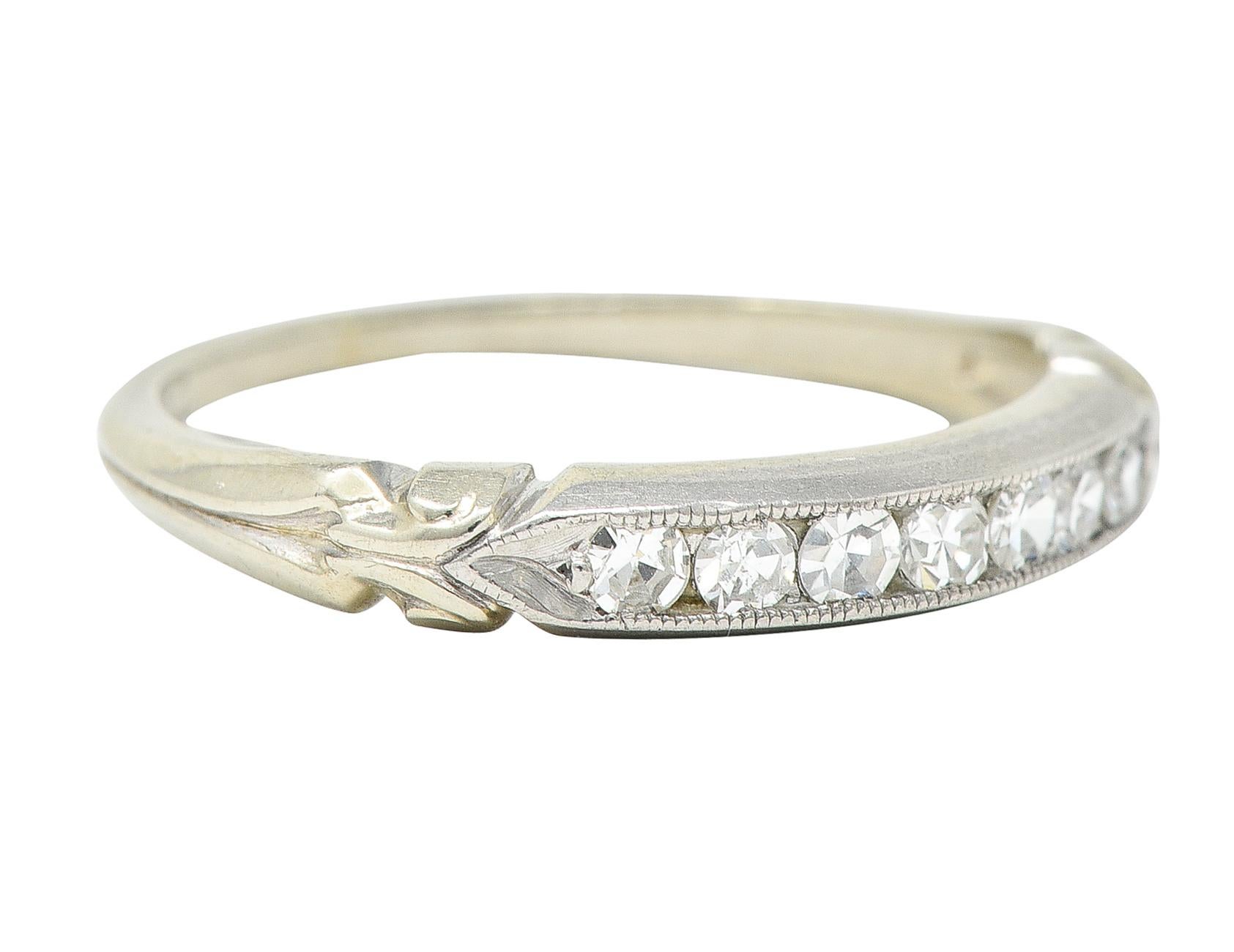Band ring features single cut diamonds weighing collectively approximately 0.25 carat - G/H color with SI clarity. Channel set to front in a platinum recess with a milgrain surround. With pointed shoulders accented by a scrolled volute motif. Subtly