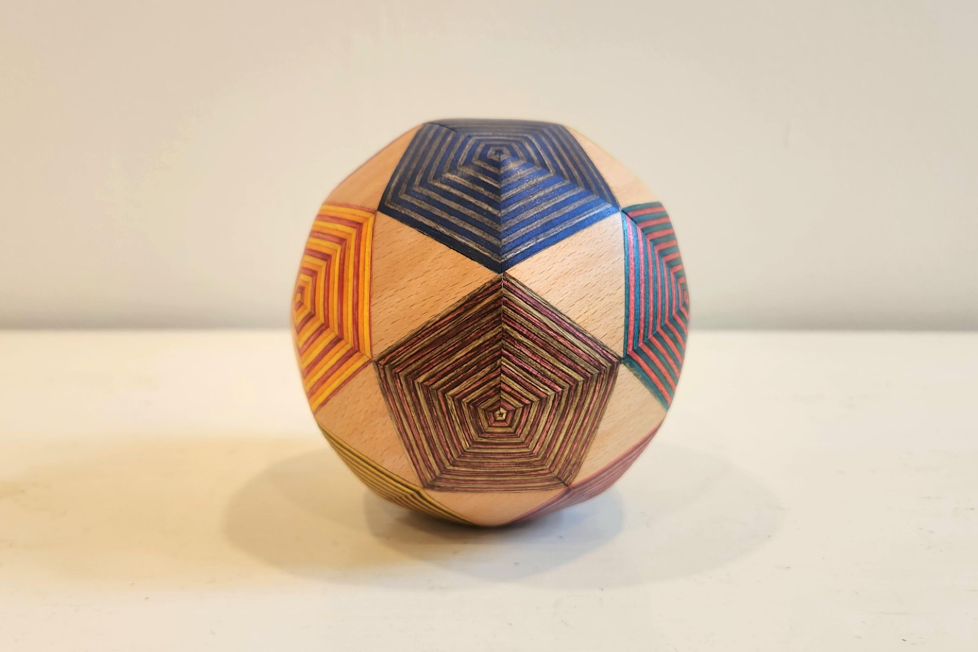 This unique sculpture is comprised of a combination of maple wood and pigmented birch plywood. This piece is comprised of 80 individual faces and is called Frequency 2 Icosahedron. This piece has an energy of playfulness to it, with the way in which