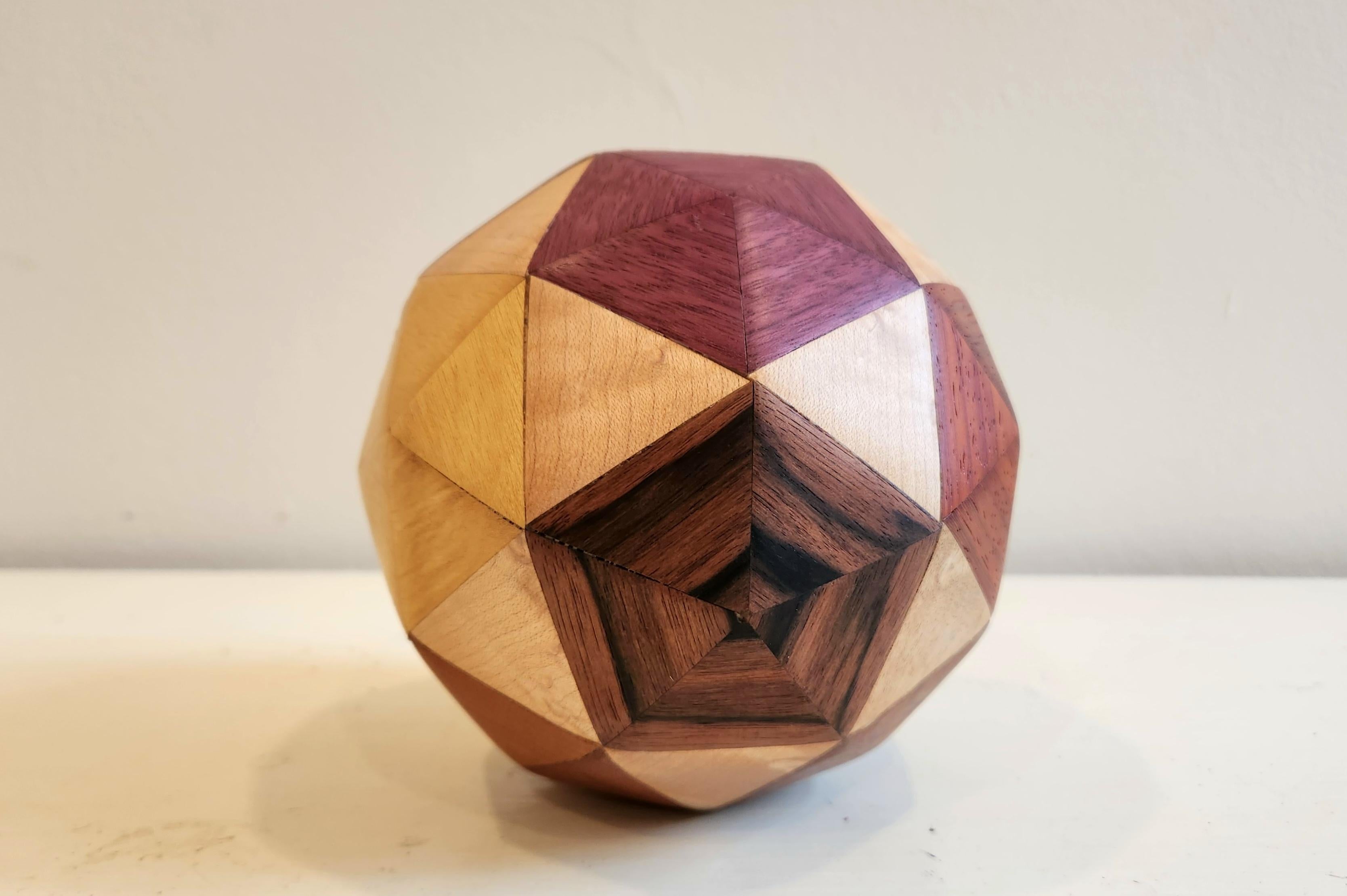 This unique piece is comprised of a variety of exotic hardwoods. This sculpture is composed of 80 individual faces, and is titled Frequency 2 Icosahedron. This work has a calm and elegant nature to it. The intense browns of the wood contrast and