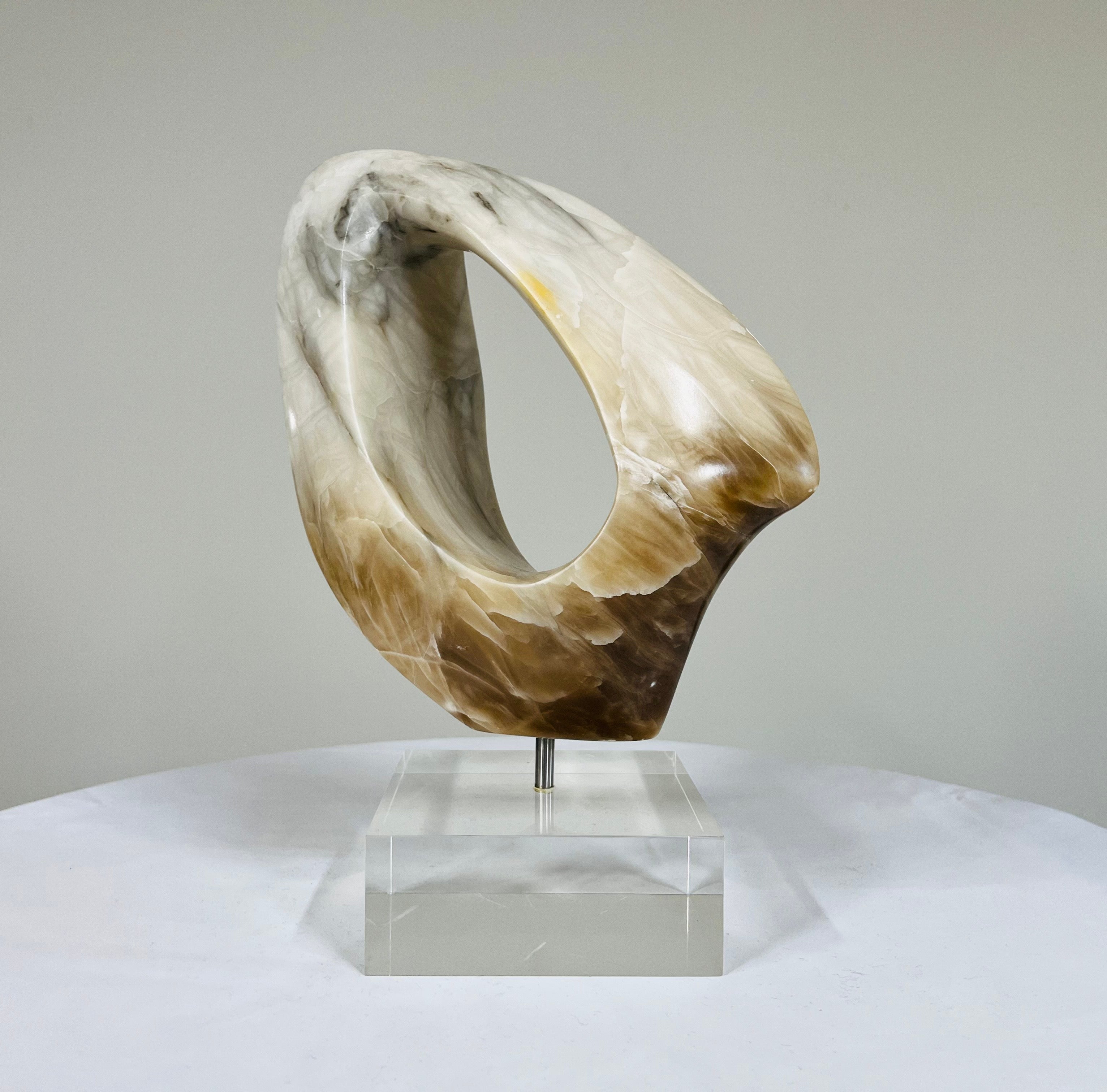 An organic alabaster stone carving over lucite stand attributed to Anthony Quinn having masterfully carved elegant lines that appear to cut a ribbon in time or perhaps the universe. The stunning grain provided by the carefully selected stone sample