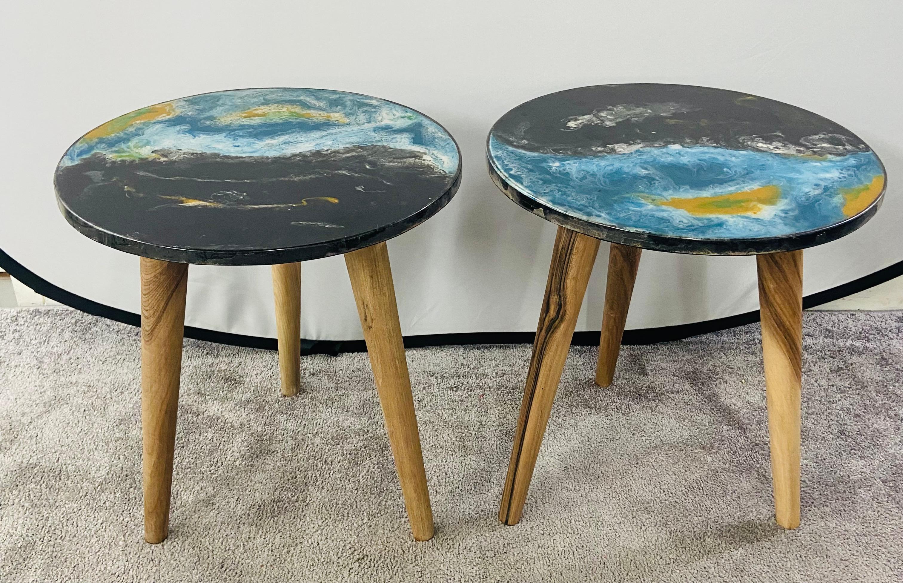 A Mid-Century Modern style pair of round top Resin Epoxy abstract design en or side table. The one of kind table top features back and blue with hint of yellow colors over three splayed pig legs made of walnut. The beautiful wood grain natural