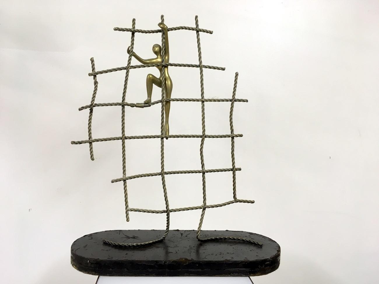 Abstract figure climbing up a net. 

Brass and nickel on black painted wooden base

circa 1960s-1970s.