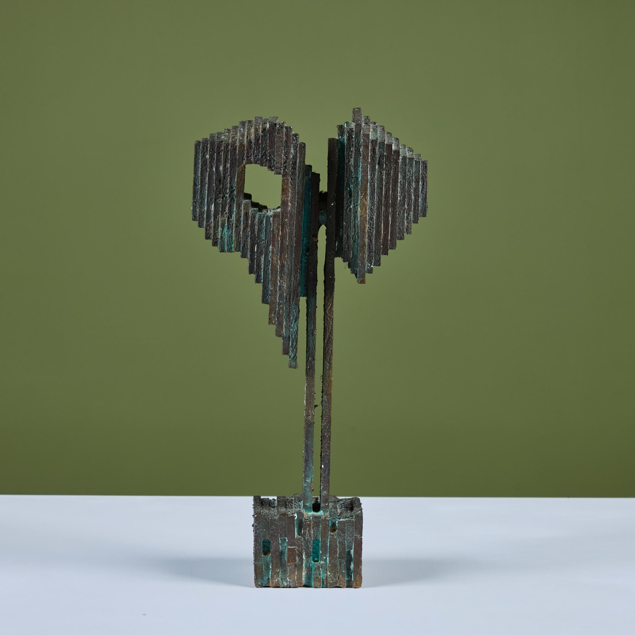 Scultura astratta montata in bronzo. La scultura presenta una base quadrata e un gambo stretto che si espande a destra e a sinistra, dando vita a un look a strati. Un lato sembra essere una piramide, mentre l'altro presenta una piccola 