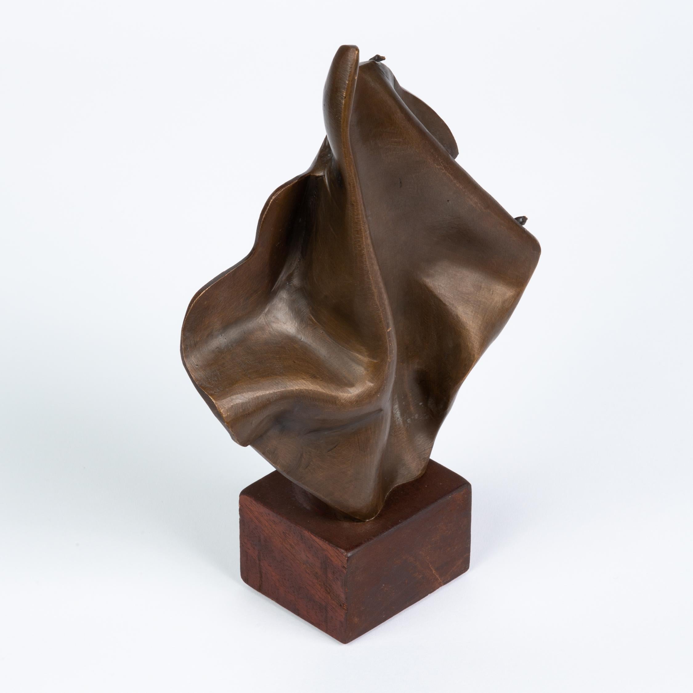 A small, abstract sculpture in cast brass, vaguely mimicking the folds of a draped cloth. The diamond-shaped, upright structure could also be meant to suggest the movement of flames. The bronze is mounted to a stained wood block, creating a