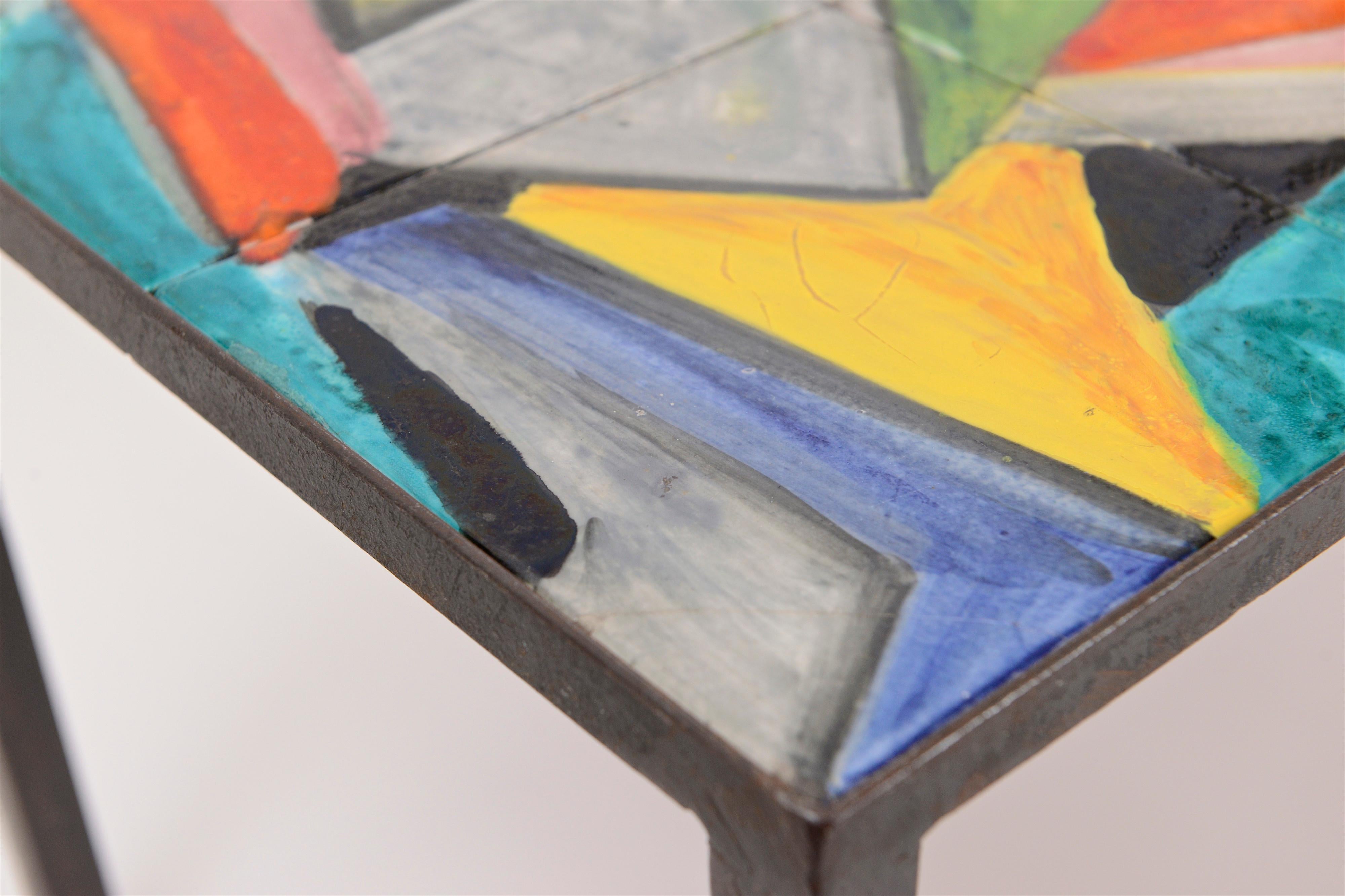 A mid-century rectangular coffee table with ten hand-painted terracotta tiles each decorated in a colourful abstract form. The decorative tiles sit flush within a black-painted steel frame with adjustable circular brass feet – a fine and unique