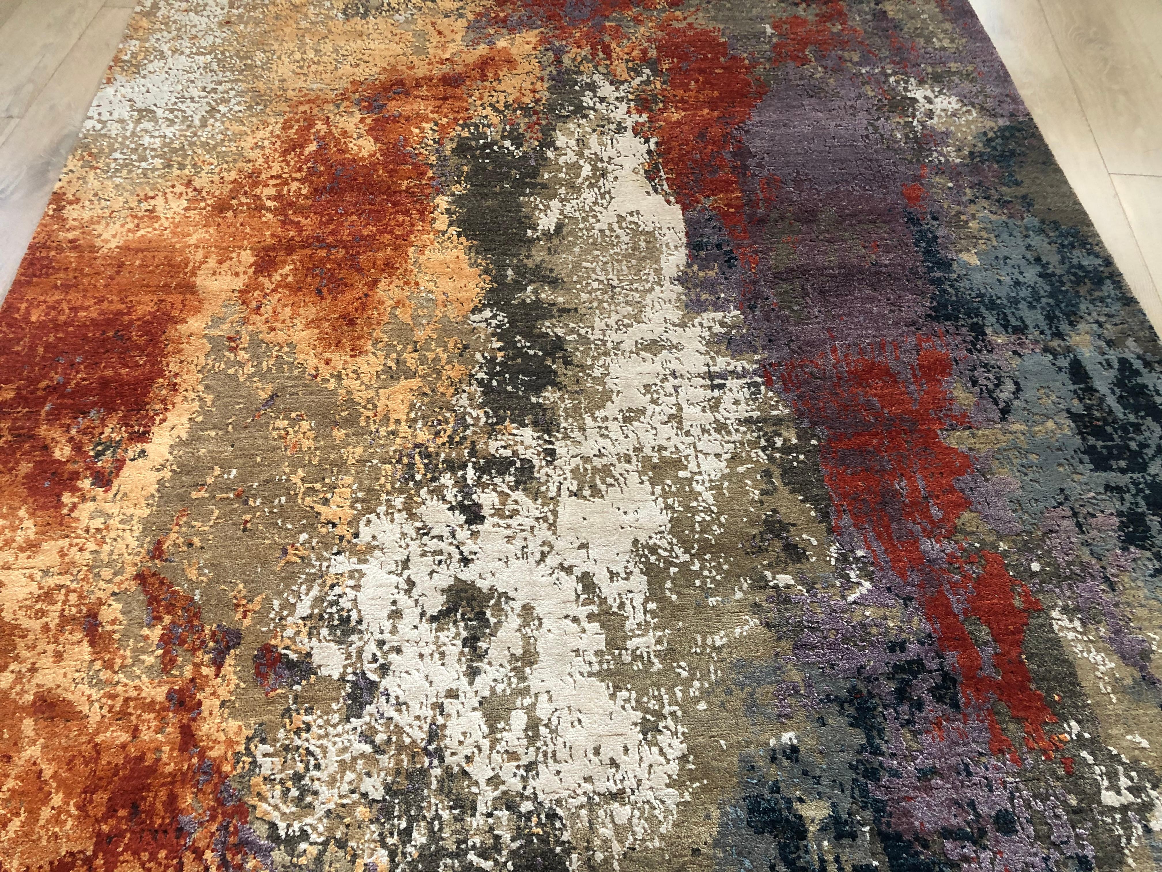 Un tappeto astratto di grande effetto, bello da vedere e morbido sotto i piedi. Un tappeto multicolore con toni dominanti di arancio, lilla, oro, beige, taupe e crema. Un misto lana/viscosa gli conferisce resistenza, morbidezza e lucentezza.