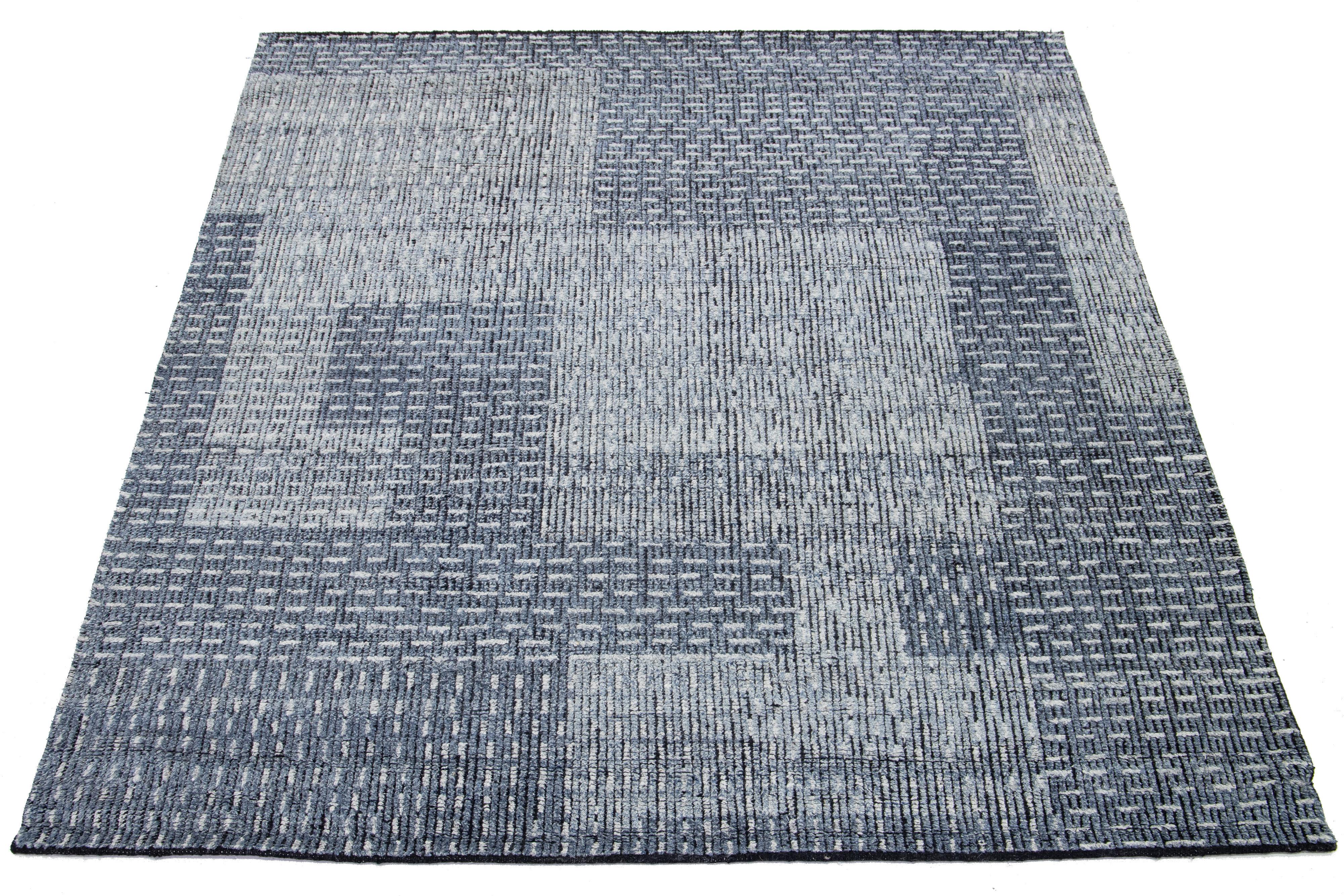 Dieser moderne, handgeknüpfte Wollteppich zeigt ein atemberaubendes blaues Feld mit einem abstrakten, geometrischen Muster.

Dieser Teppich misst 8'1