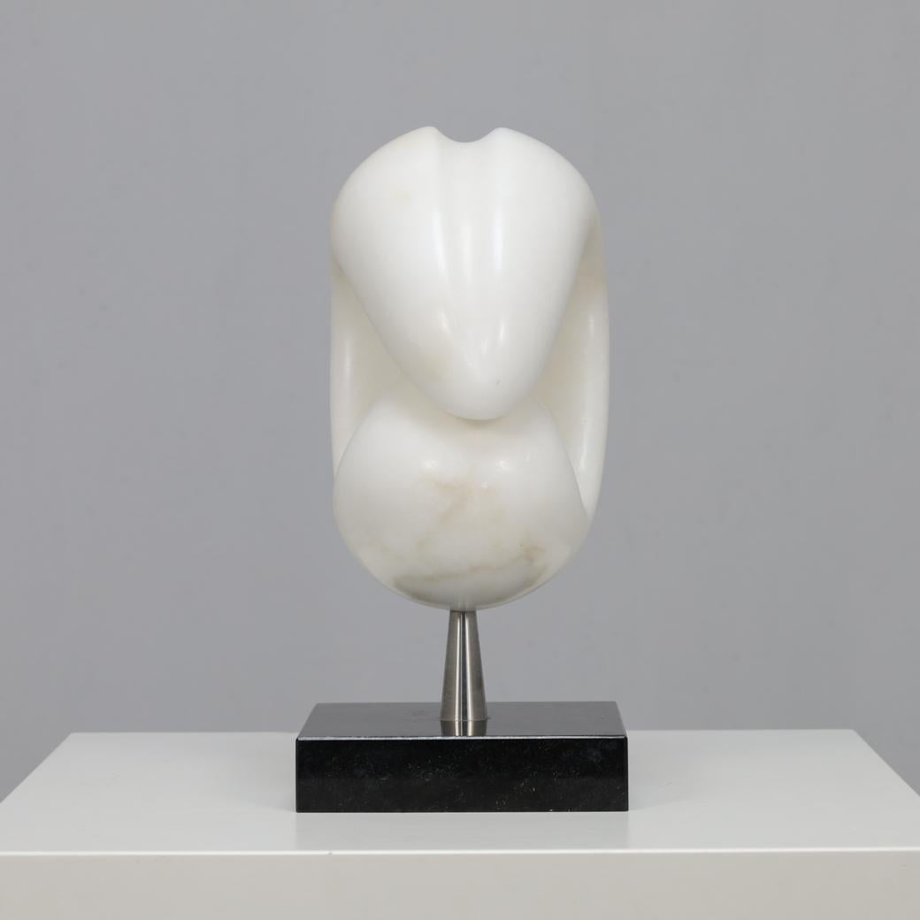 Una llamativa escultura abstracta de mármol blanco tallado a mano, montada sobre un pasador de acero inoxidable y una base de piedra oscura. La obra expresa una serena tensión entre el movimiento orgánico y la precisión arquitectónica, sello