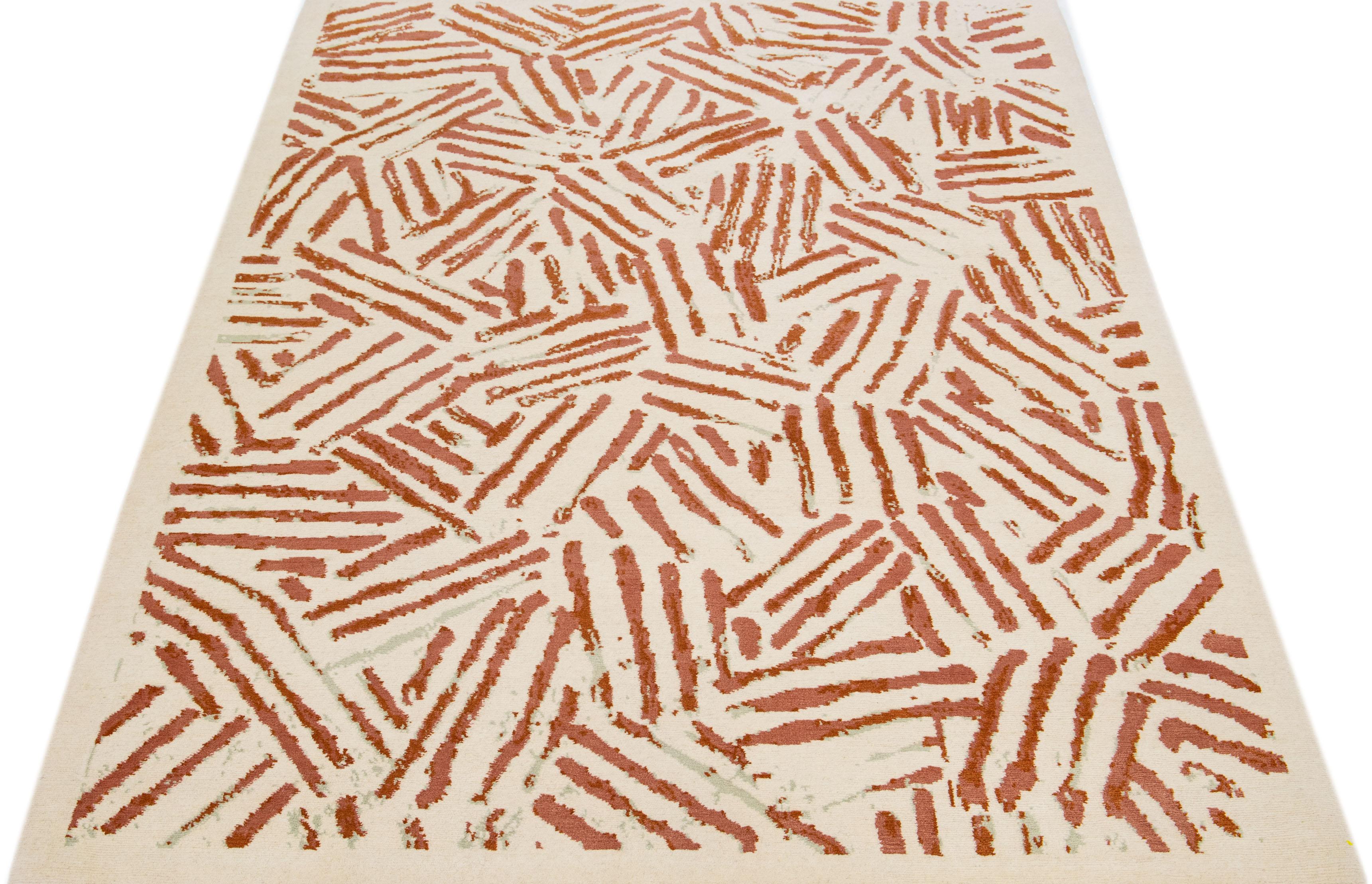 This Tibetan rug boasts a contemporary abstract design made of high-quality wool, hand-knotted to perfection. The ivory backdrop features a striking all-over geometric pattern, accentuated with rust-colored highlights for added richness and