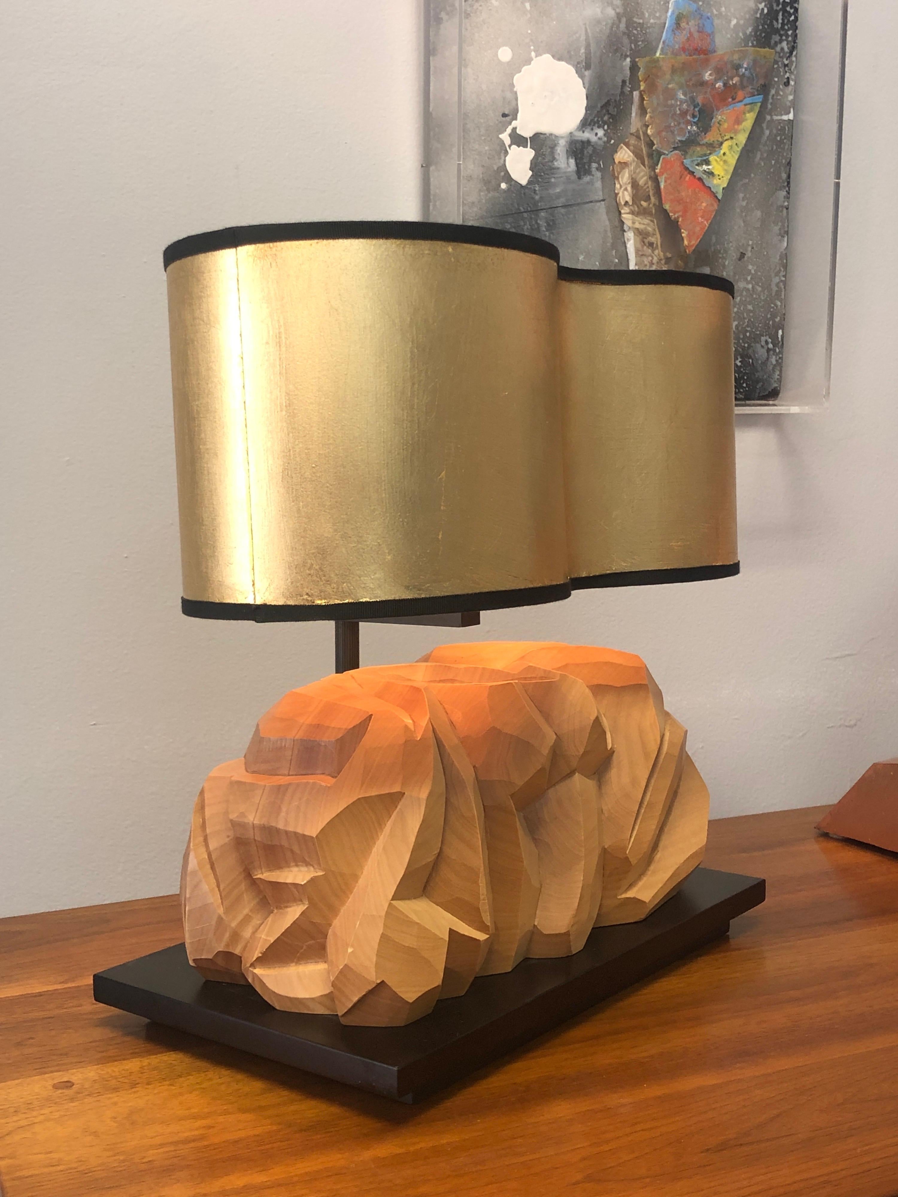 Una lampada da tavolo di grande effetto. Una grande scultura in legno chiaro intagliata a mano, realizzata in stile organico, poggia su una base nera. Ferramenta in bronzo, conserva il paralume originale dorato a forma libera.