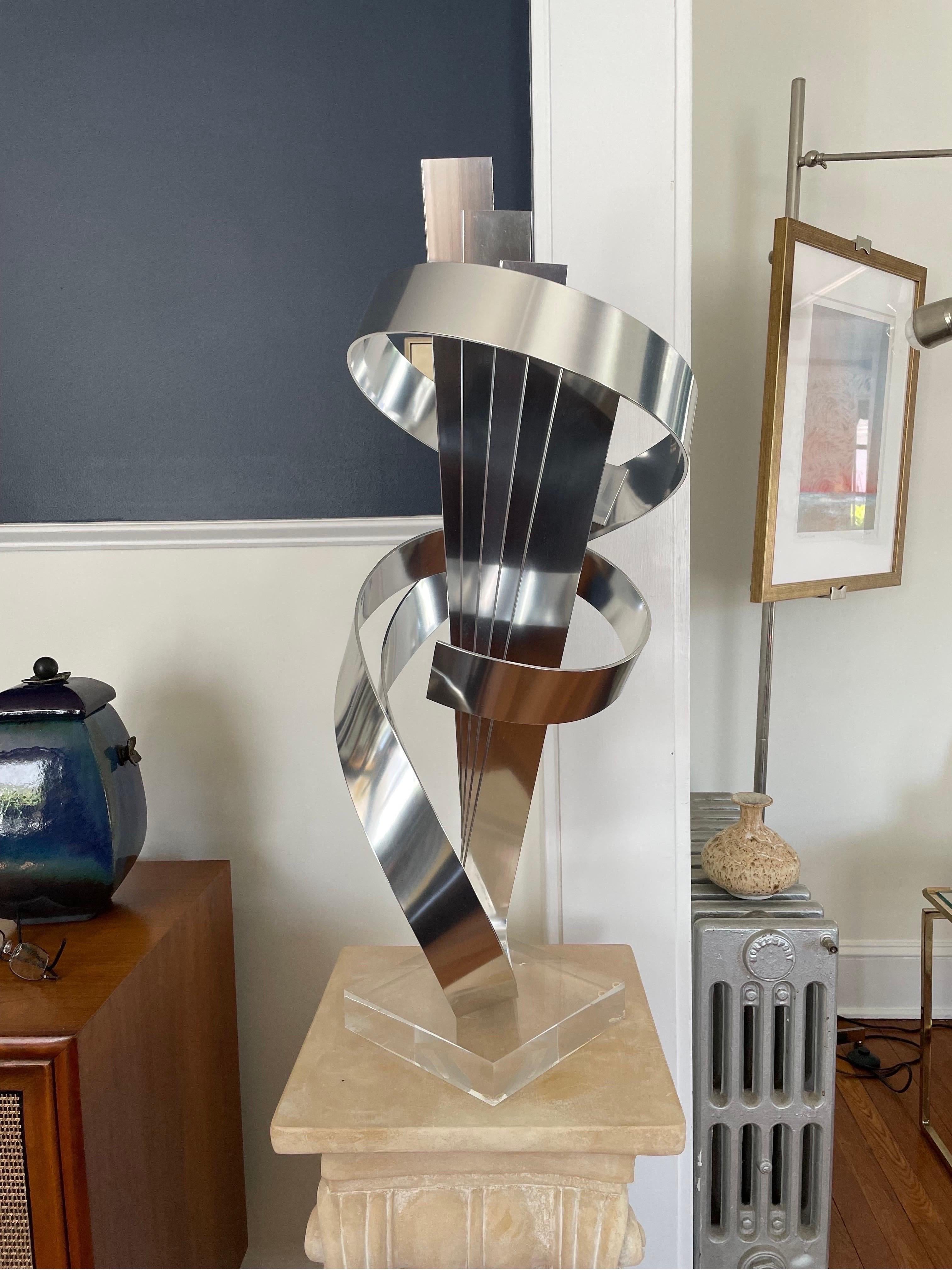 Spectacular presence with this Ribbon Sculpture by Dan Murphy. Unique design with 5 fanned ribbons encircled by a 2 ribbon swirl. Beautiful polished steel set on lucite base. 

Curbside to NYC/Philly $350.