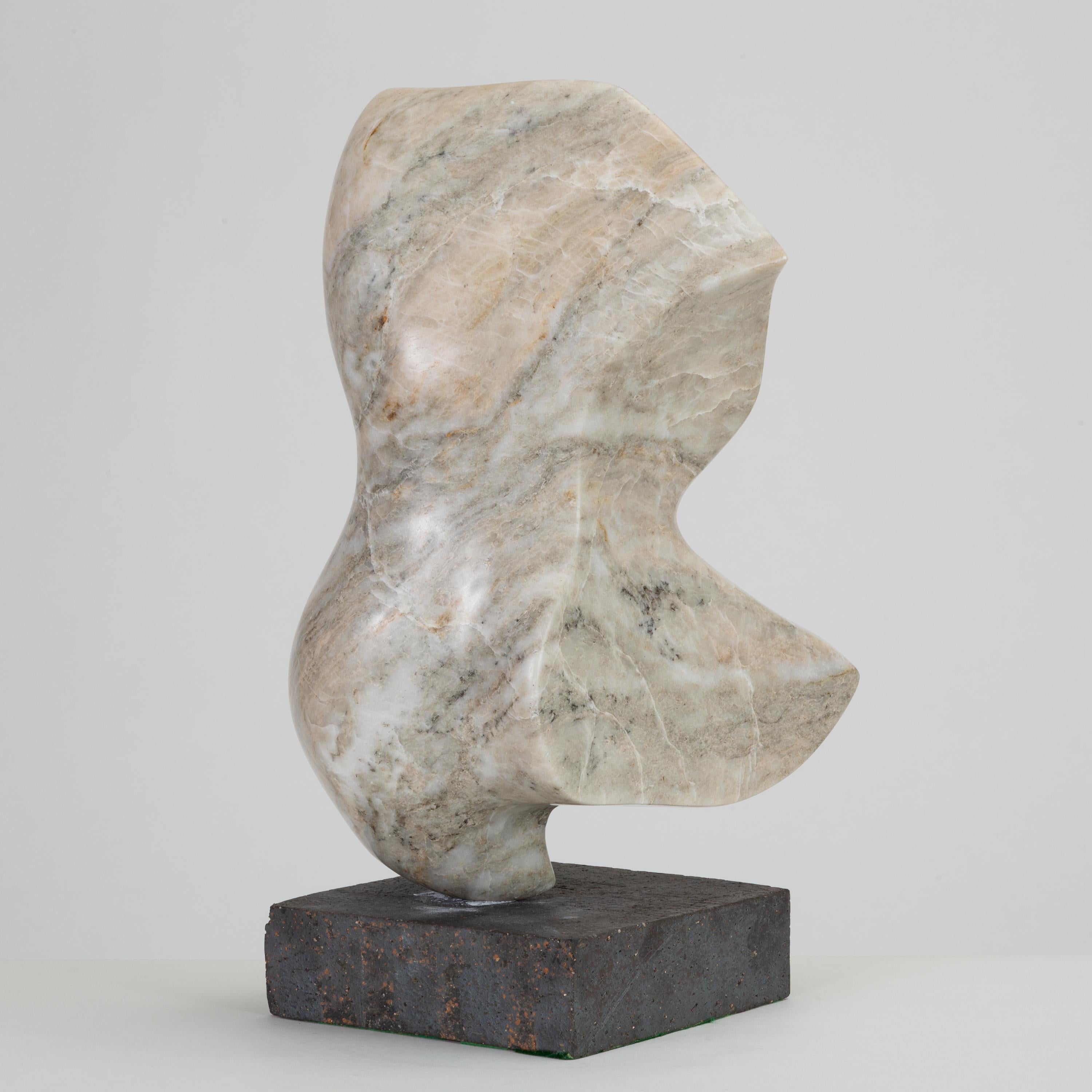 A gray marble sculpture, touched with notes of ochre and cinnamon. The abstracted form, mounted on a gray brick base, has a biomorphic form, with subtle veining in blush and charcoal following the curves of the figure. 

Condition: Excellent