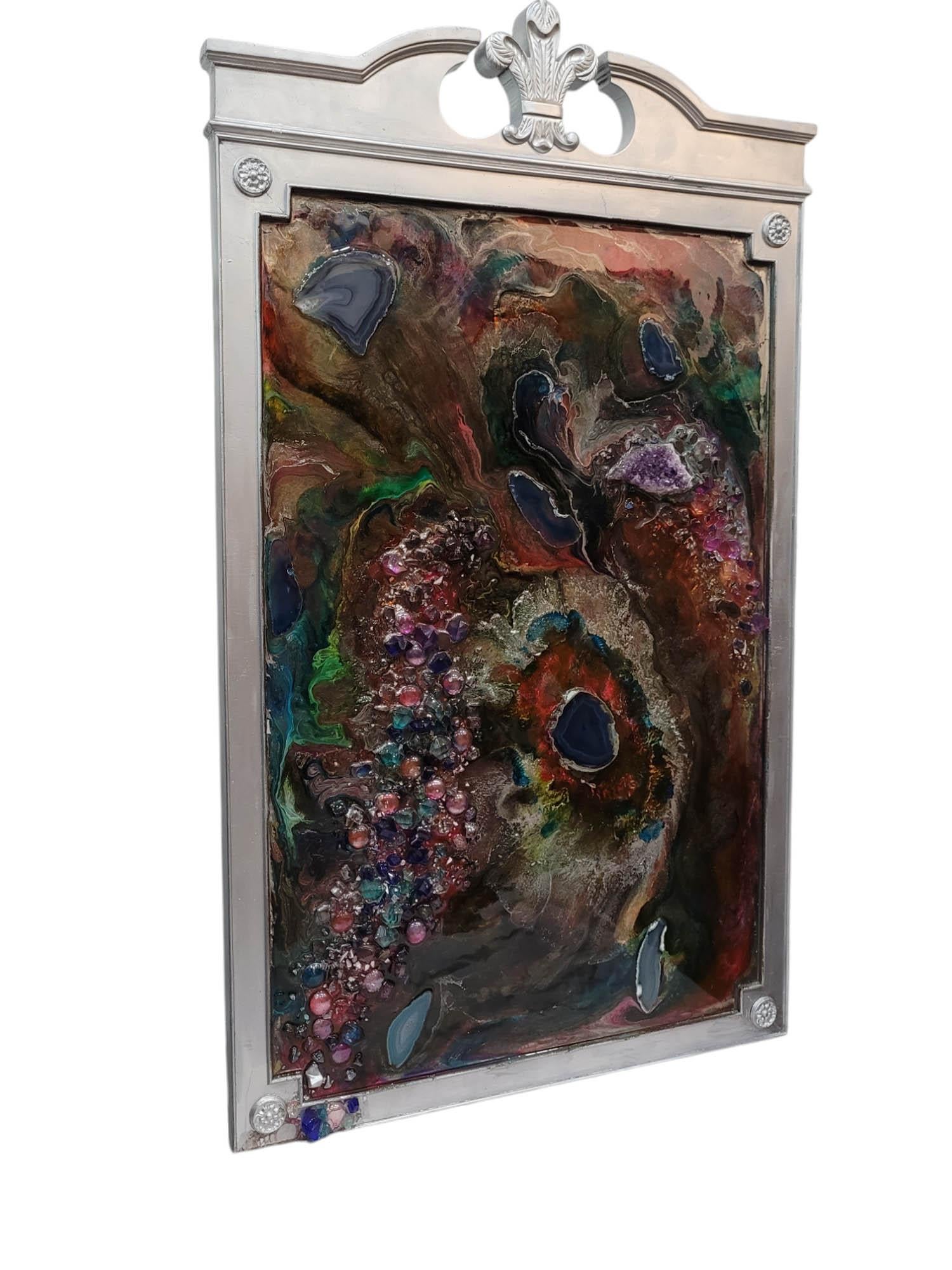 Dieses Mixed-Media-Kunstwerk ist eine fesselnde Verschmelzung von natürlicher Schönheit und abstraktem Ausdruck. Es ist in Silber mit einem Fleur-de-Lis-Motiv gerahmt und zeigt eine wirbelnde Komposition aus Edelsteinen und Farbe, die an natürliche