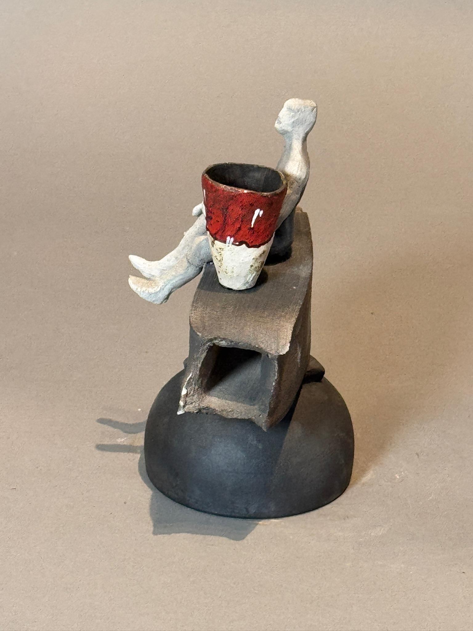 Esta llamativa escultura de cerámica moderna combina el arte abstracto con una narrativa contemplativa. Con una figura humana minimalista encaramada a una base geométrica, la pieza emana equilibrio y serena reflexión. El recipiente rojo y blanco que