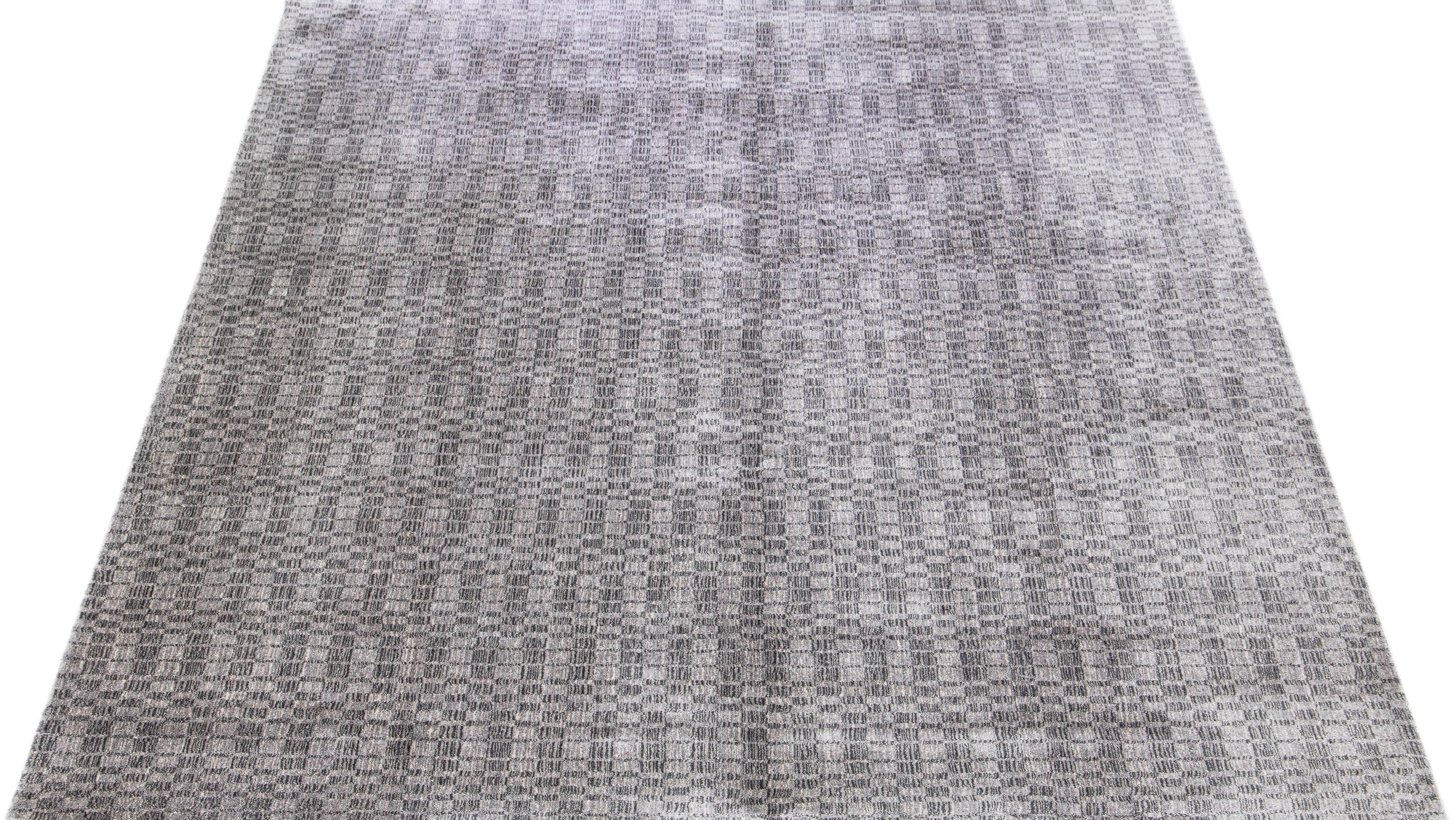 Dieser exquisite zeitgenössische Teppich, der in sorgfältiger Handarbeit aus einer Mischung aus Seide und Wolle gefertigt wurde, zeigt ein atemberaubendes graues Grundmuster, das durch ein verführerisches geometrisches Design in Silberschattierungen