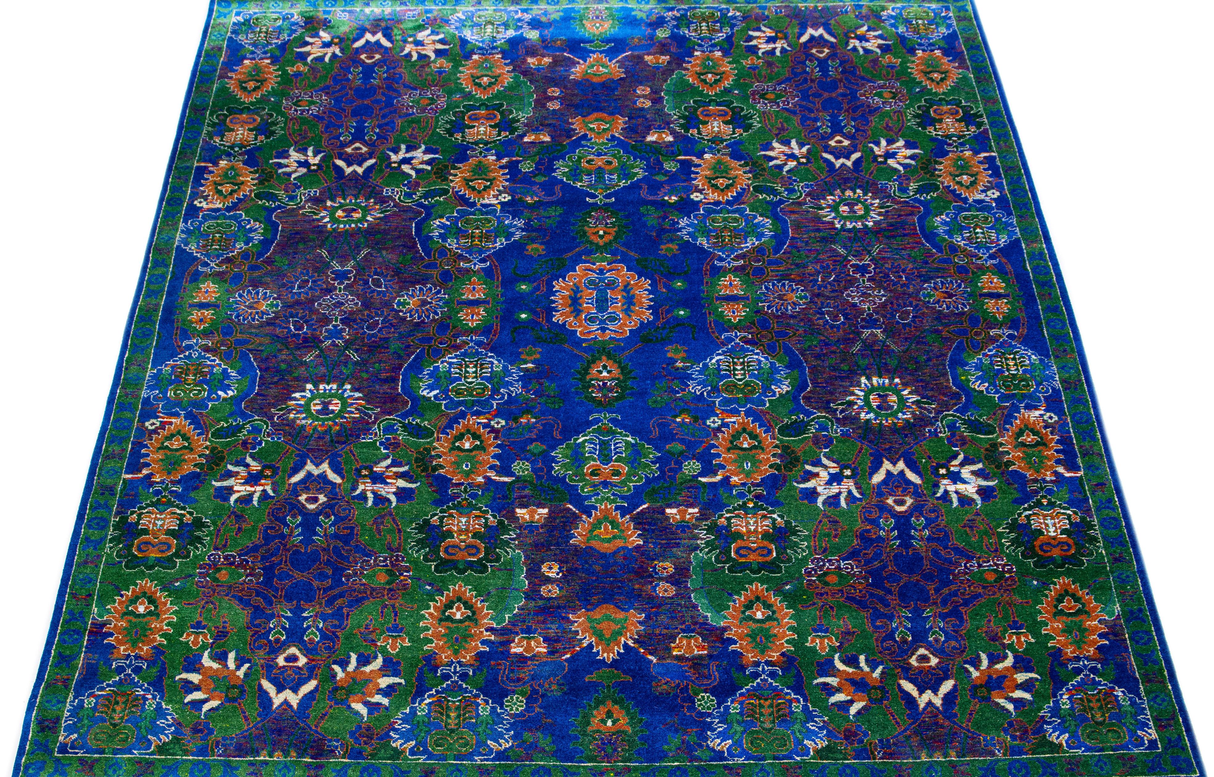 Dieser luxuriöse, raffiniert gewebte Flächenteppich ist eine Mischung aus indischer Wolle und Seide. Der blaue Hintergrund ist mit einem eleganten Blumenmuster verziert, das mit grünen und orangefarbenen Farbtupfern für einen kräftigen Farbakzent