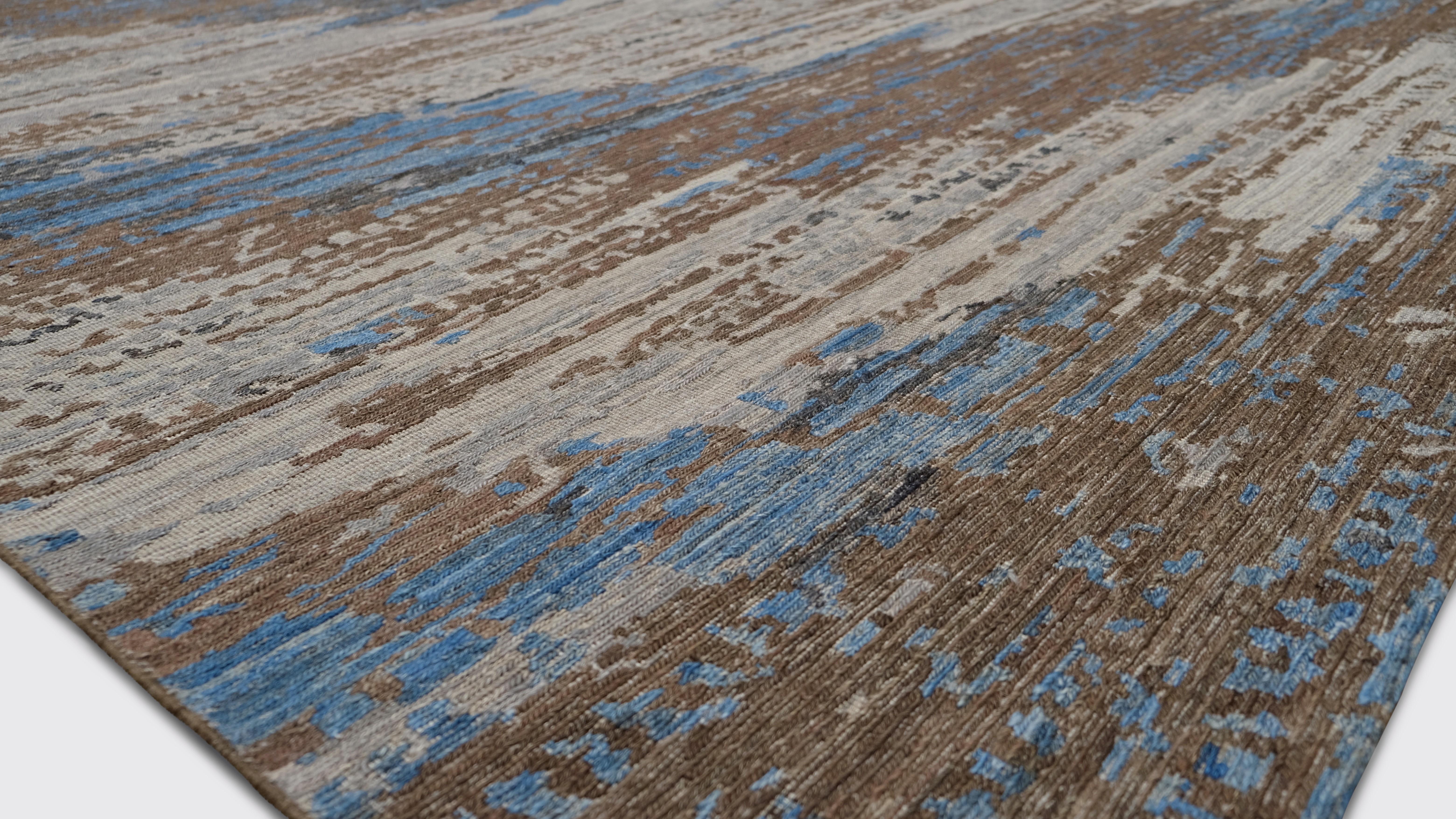 Introduce el arte orgánico en tu hogar con esta alfombra de lana anudada a mano, con un diseño abstracto inspirado en la tierra y el cielo en tonos azul, marrón y marfil. La mezcla dinámica de tonos fríos y cálidos evoca una sensación de armonía